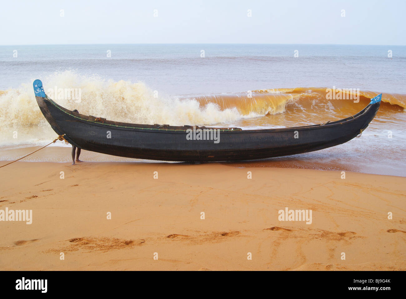 Fisherman legato la sua imbarcazione in legno sulla riva.furiosa ruggenti onde del mare rendono il suo lavoro molto duro.scena dalla costa di pesca del Kerala Foto Stock