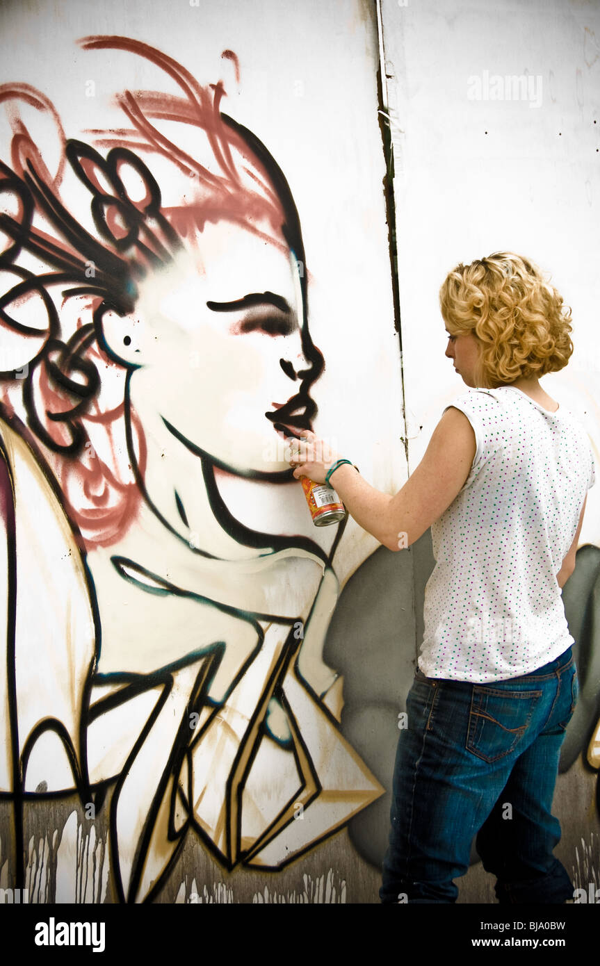 Vista posteriore del giovane artista graffiti femmina caucasico adulto con bomboletta di vernice spray in mano, creando un pezzo di Street art. Foto Stock