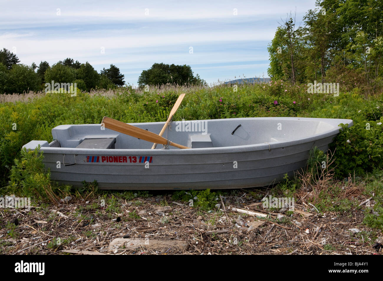 Plastica barca a remi con remi sat in un campo di erbacce Foto Stock