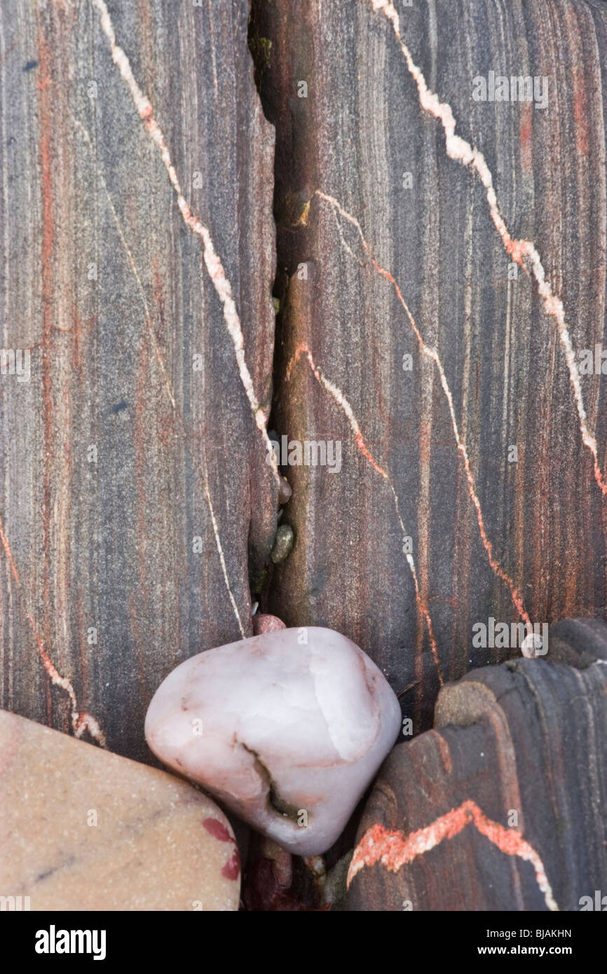 Un liscio bianco ghiaia di quarzo contro una roccia incrinato con bianco e rosa vene di quarzo Foto Stock