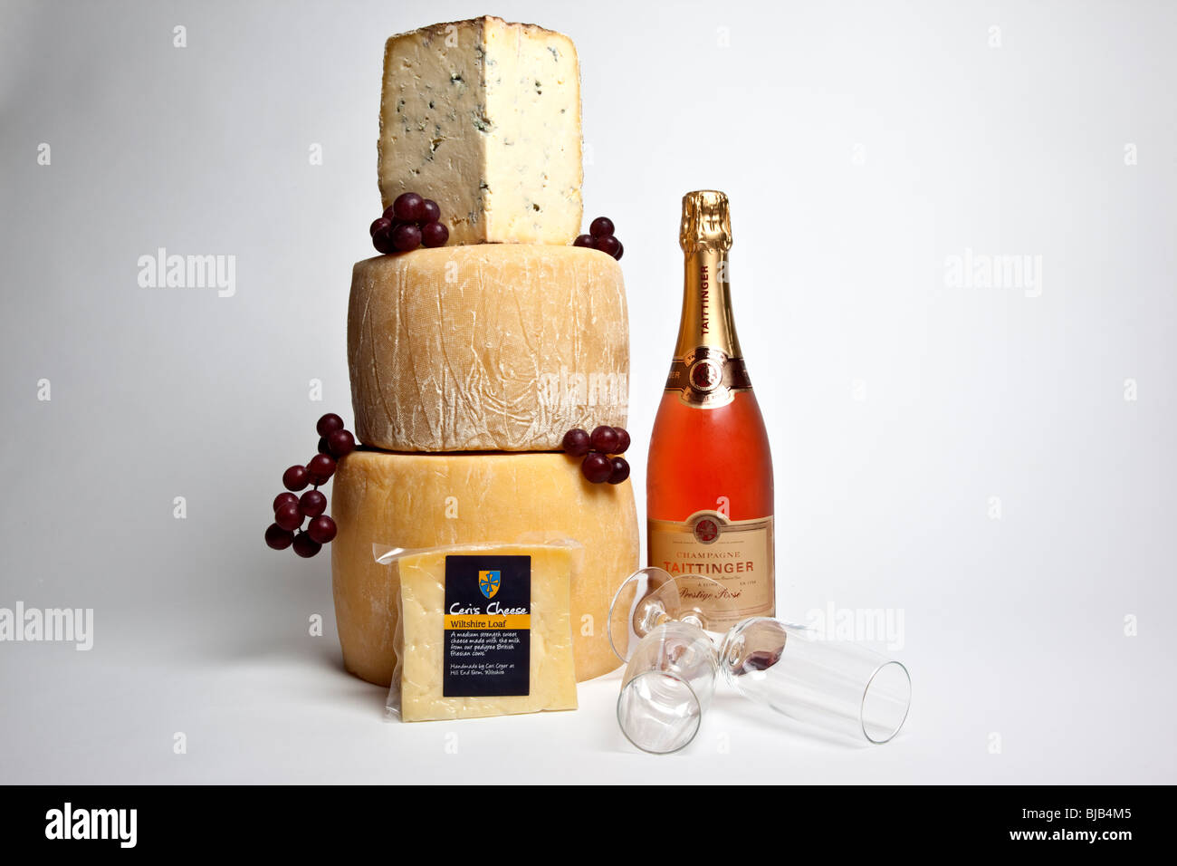 Una celebrazione torre di tutto il round di formaggi con una grande fetta di formaggio blu con una bottiglia di champagne rosato e due bicchieri Foto Stock