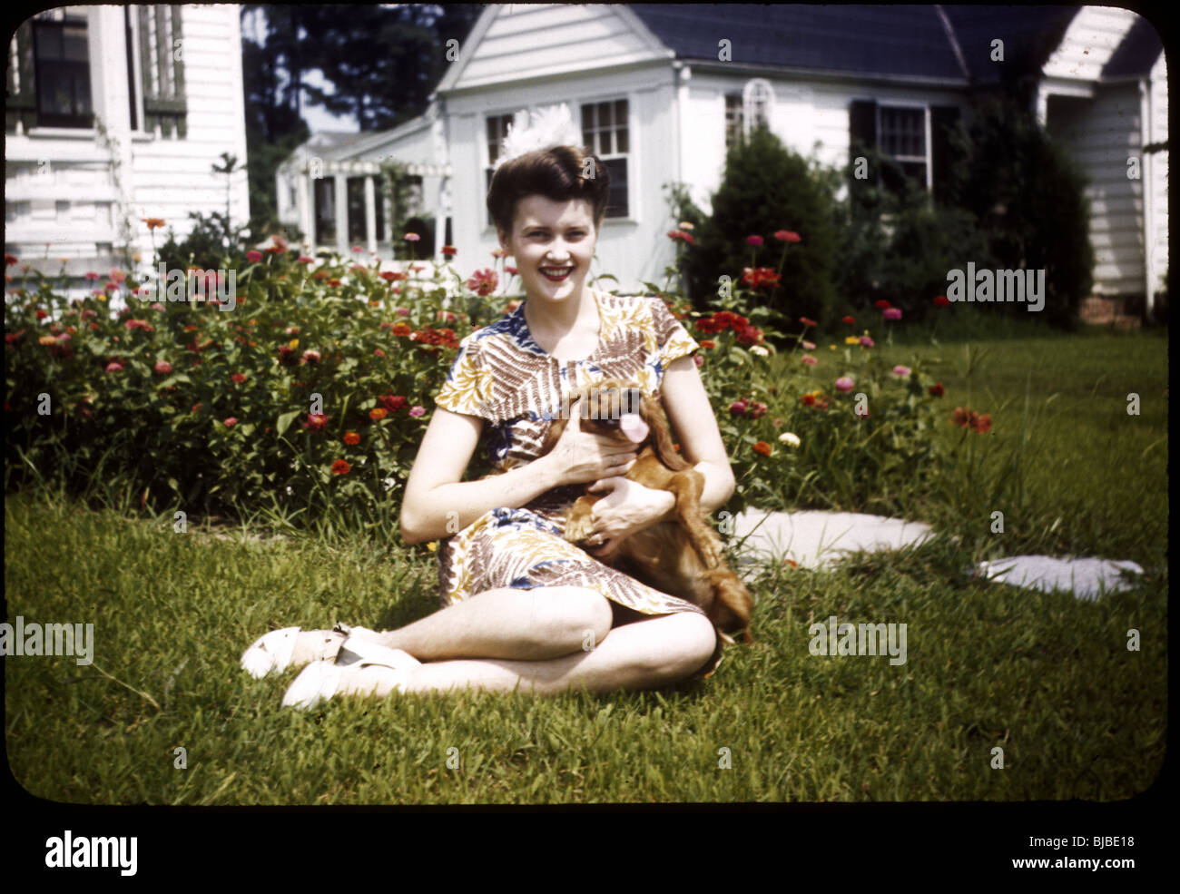 Donna con cane indossando 1940s stampa abito con cane da compagnia. 1945. Prato casa fiori primavera estate diapositiva a colori Foto Stock