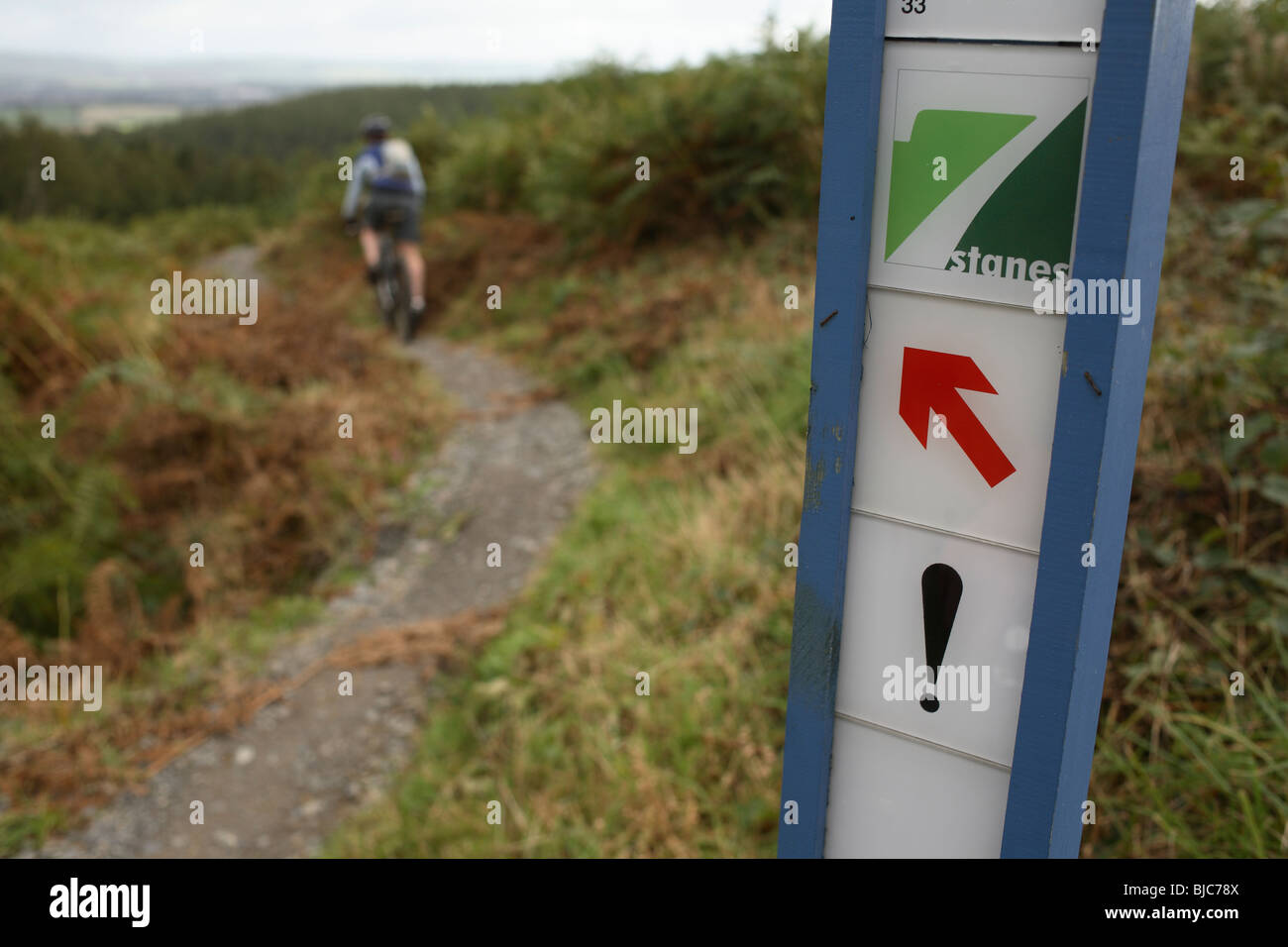 Mountain Biker passa su un cartello di avviso su un 7stanes trail in Scozia Foto Stock