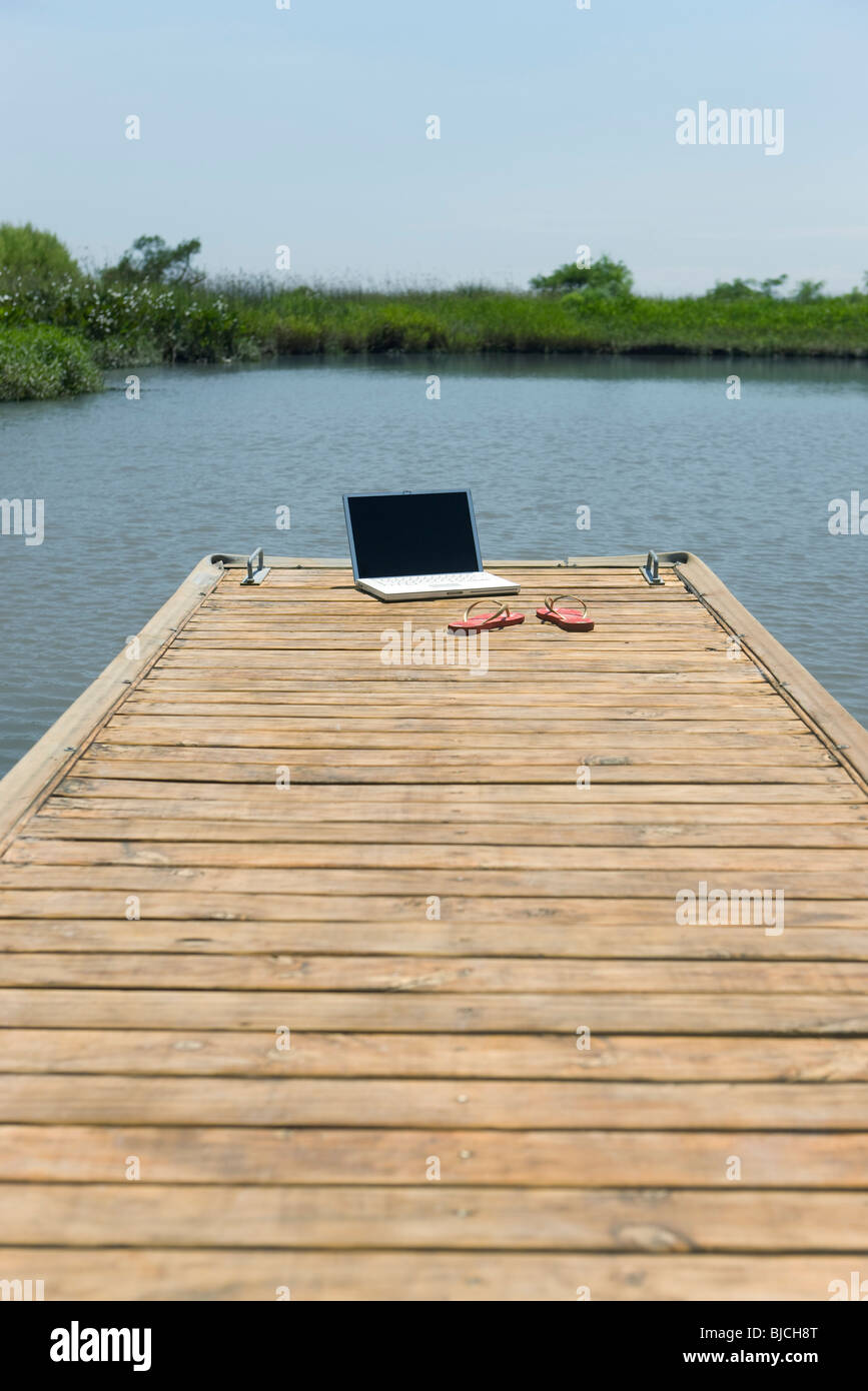 Computer portatile e flip-flop a sinistra sul dock Foto Stock