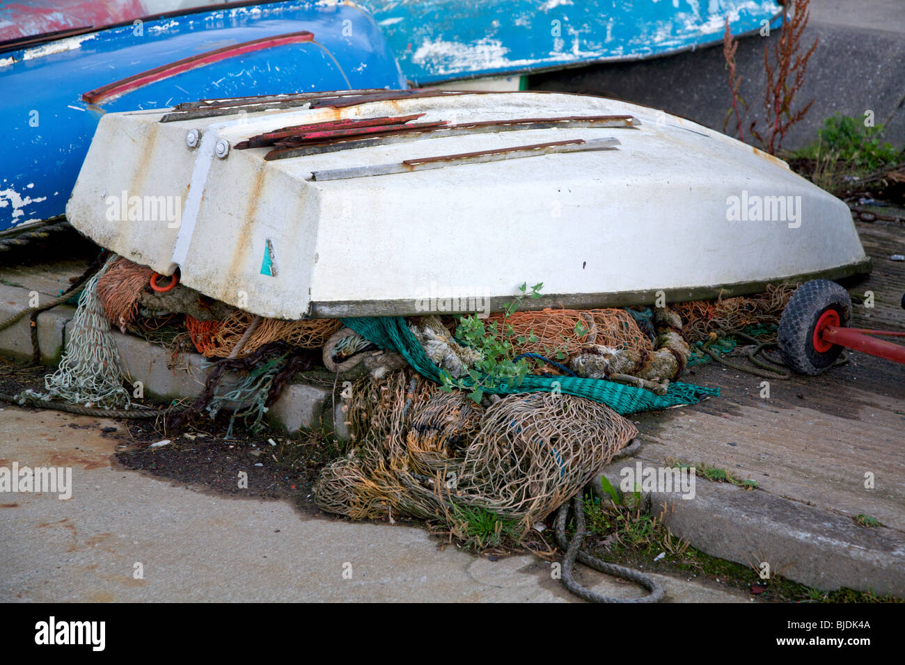 Piccole barche di gara capovolto che copre le reti da pesca a lato della strada di uno scalo Foto Stock