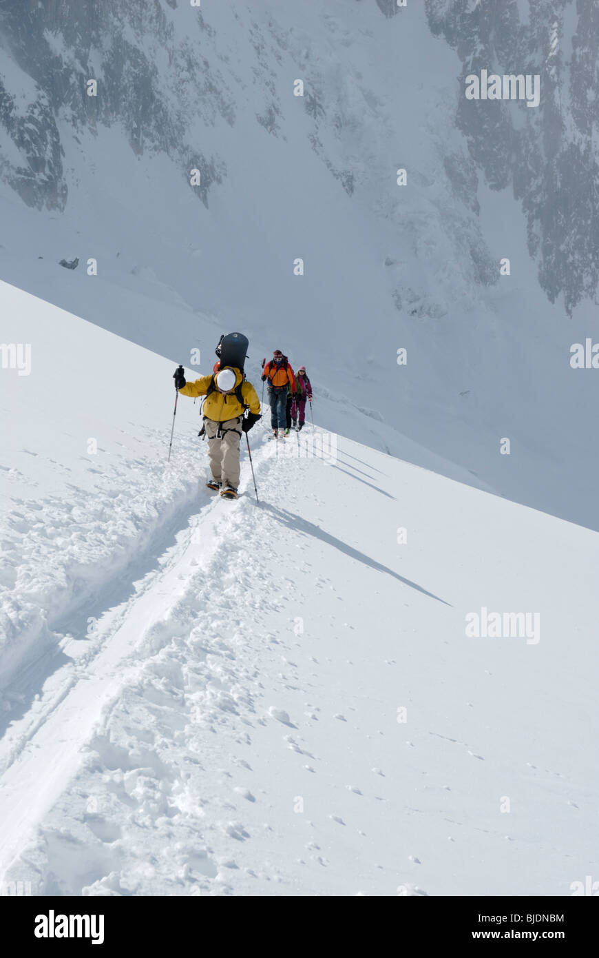 Snowboarder e sciatori salendo un pendio nevoso in terreno ghiacciate sopra la Vallee Blanche, Chamonix, Francia Foto Stock