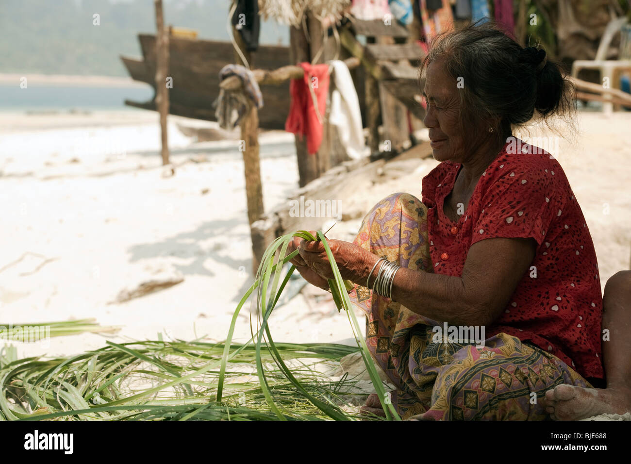 Un antico mare Moken-gypsy lady, i cacciatori-raccoglitori nomadi del Myanmar coast tessitura sulla riva Foto Stock