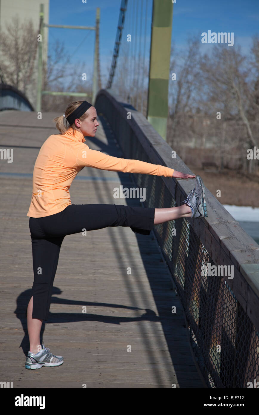 Donna runner che si estende all'aperto sul ponte pedonale nel parco cittadino Foto Stock