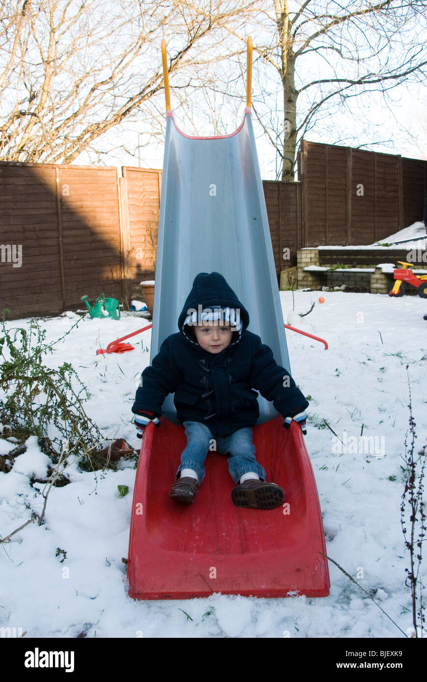 Little Boy Toddler giocando su una slitta nel retro del giardino di neve il giorno di Natale, Sheffield 2009 Foto Stock