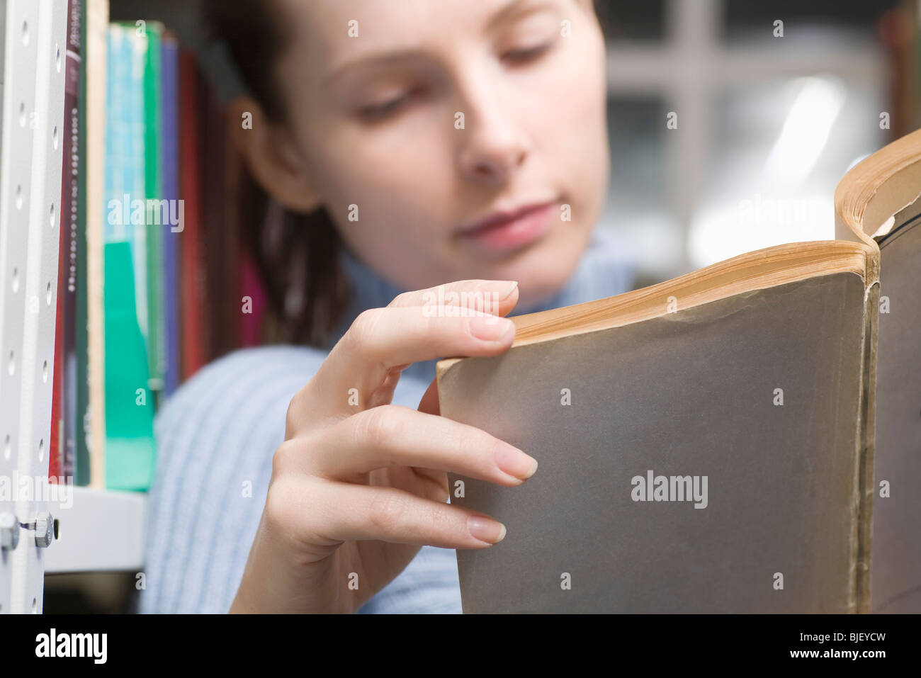 Giovane donna legge libro in biblioteca Foto Stock