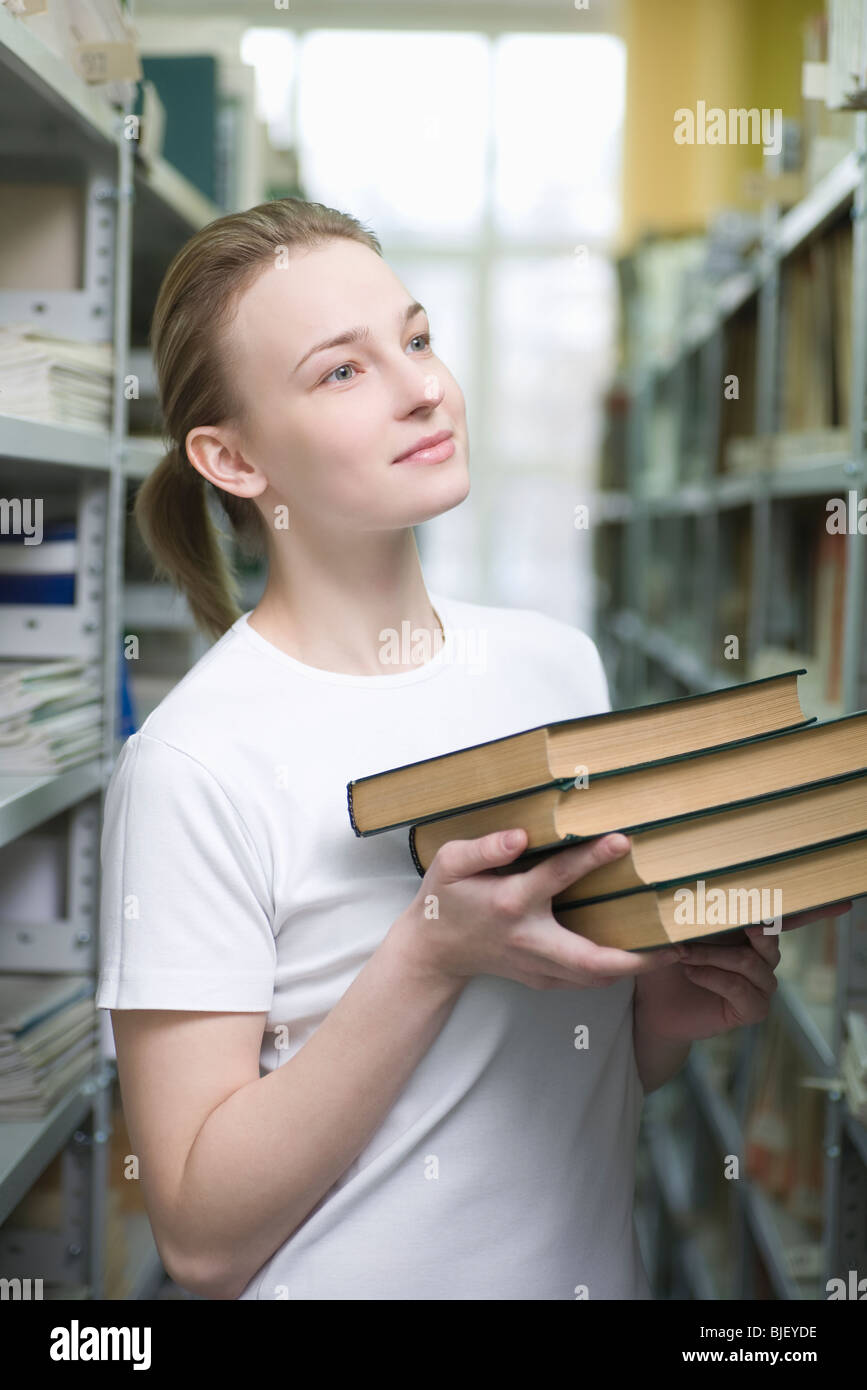 Giovane donna restituisce i libri della biblioteca a ripiani Foto Stock