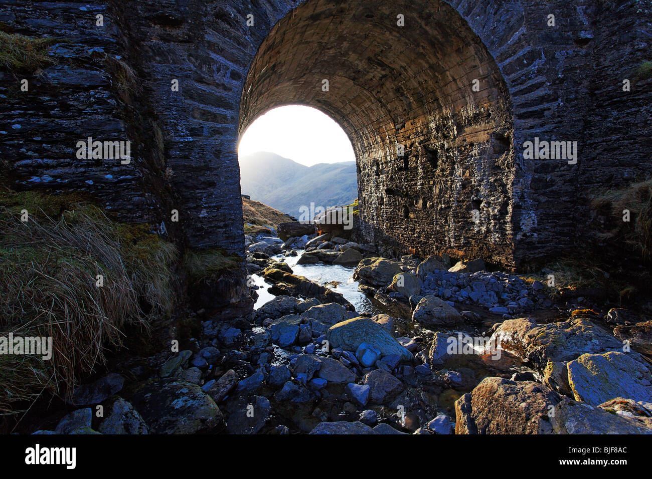 Chiudere la foto del ponte ad arco oltre il torrente di montagna che mostra la luce di contrasto Foto Stock