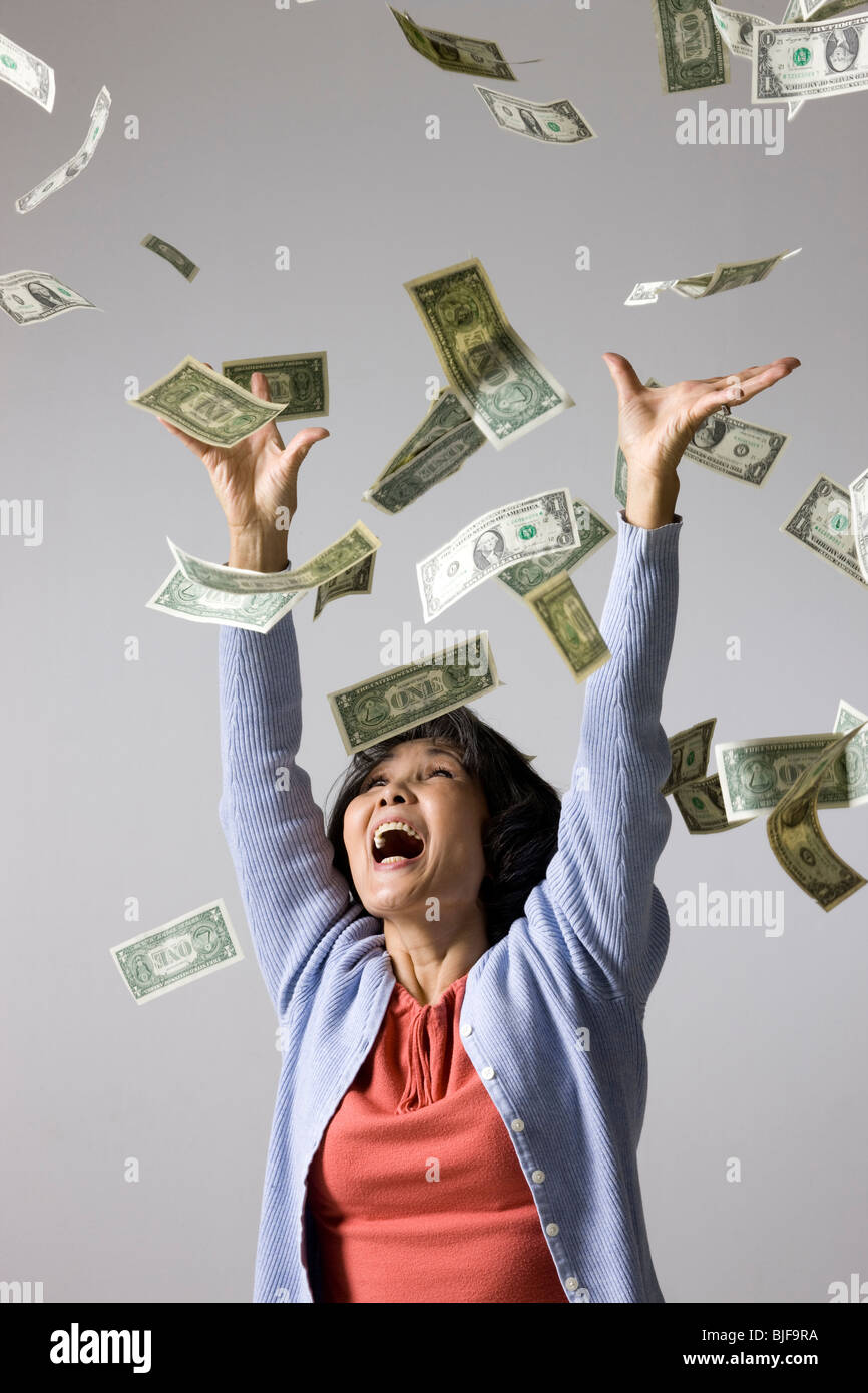 Senior donna con denaro cadere intorno a lei Foto Stock