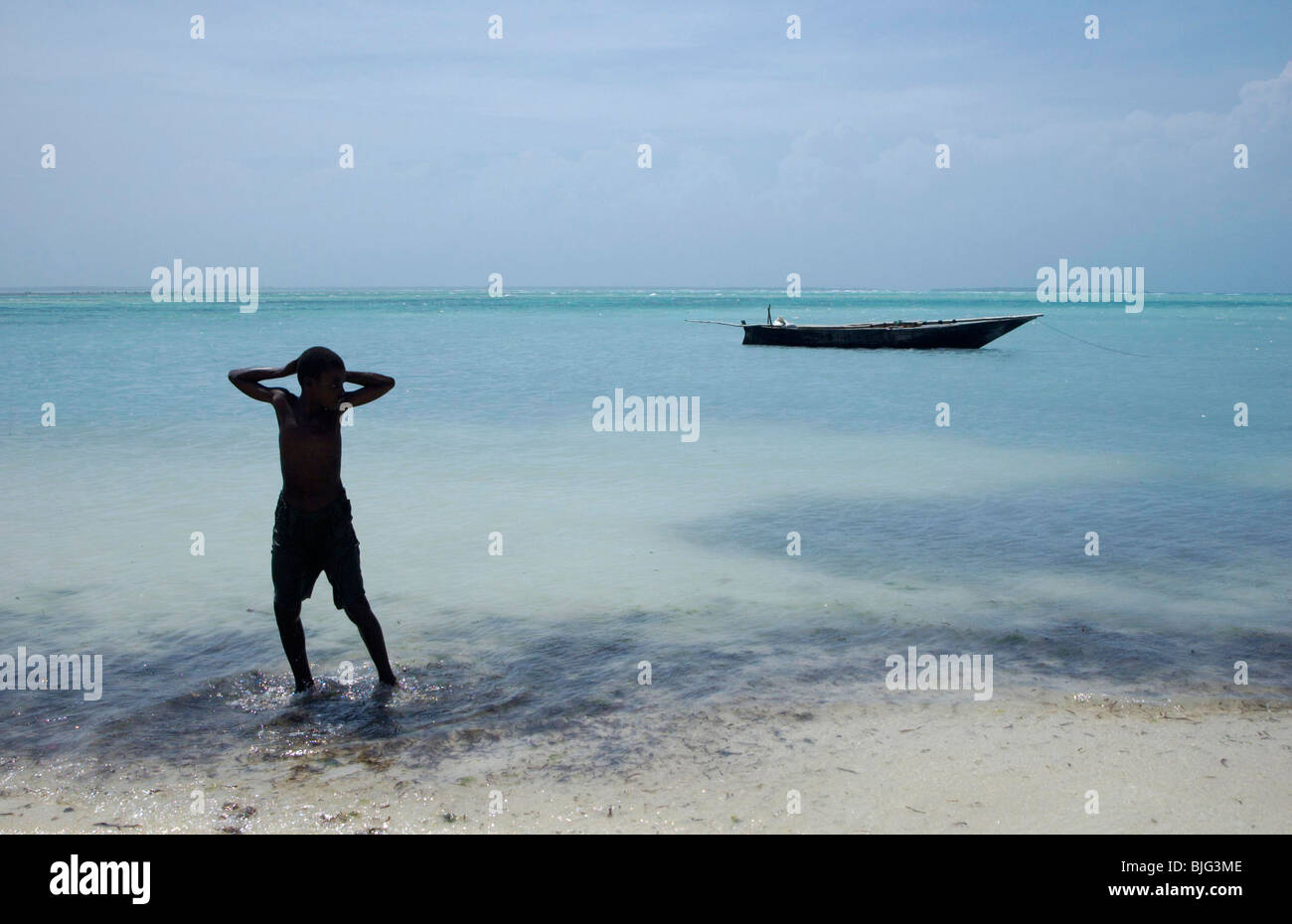 Un ragazzo giovane attende con la sua barca da pesca sulla spiaggia di Nungwi. Zanzibar, Africa © Demelza scusa Foto Stock