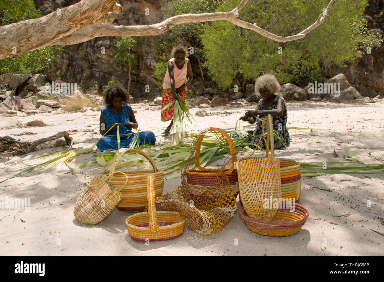 Aboriginal artigiane in dry creekbed pandanus sdoppiamento di colorante secca e intreccio cesti & dilly-sacchetti per la vendita a Injalak Foto Stock