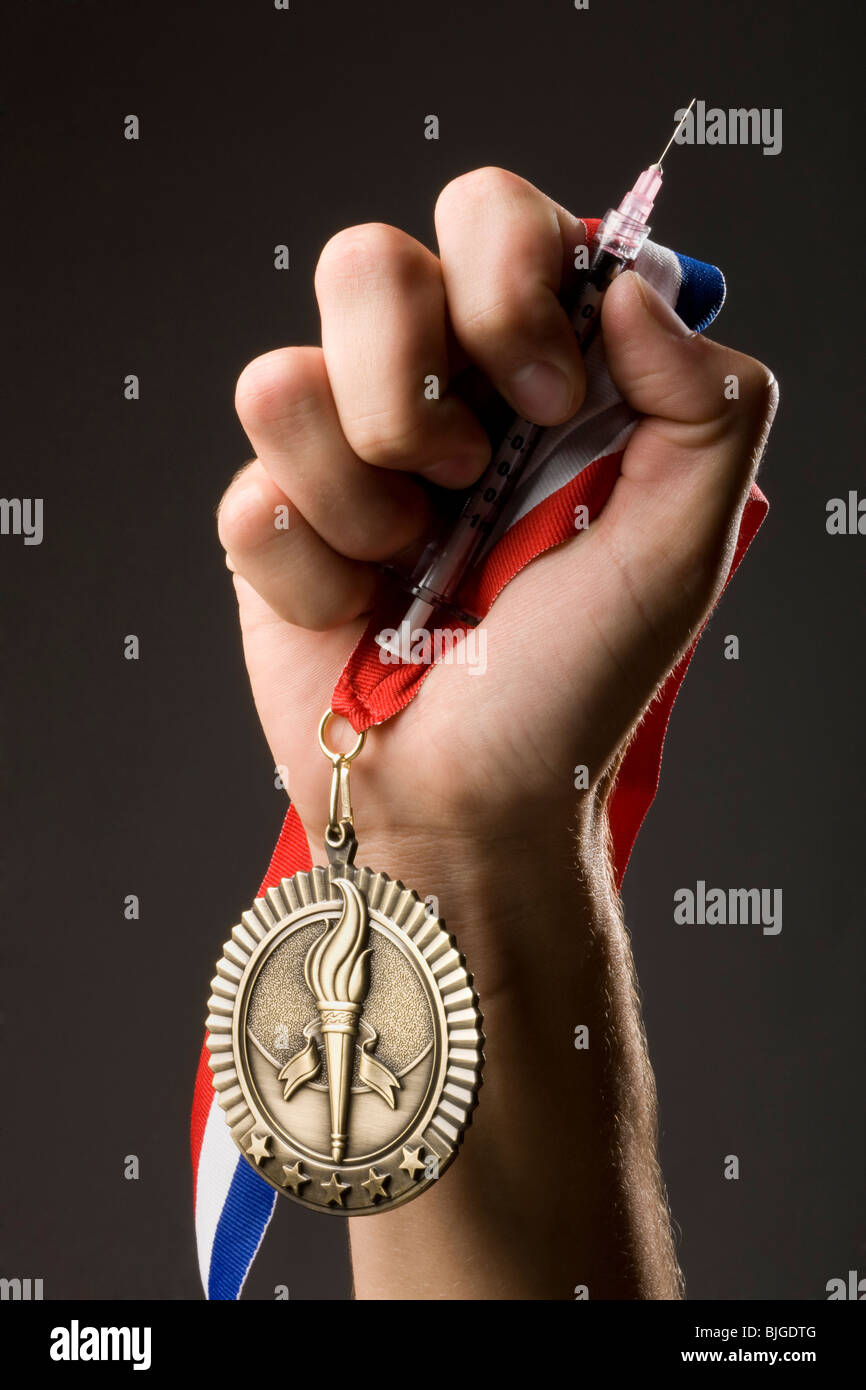 Mano che tiene una medaglia d'oro e una siringa Foto Stock