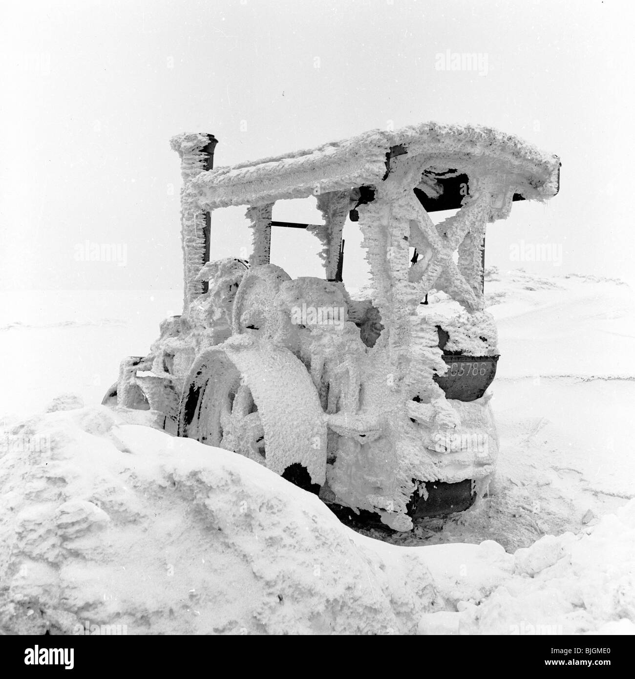 Inghilterra, 1950s. La neve copre completamente un trattore a Taylor Woodrow sito in costruzione. Foto Stock