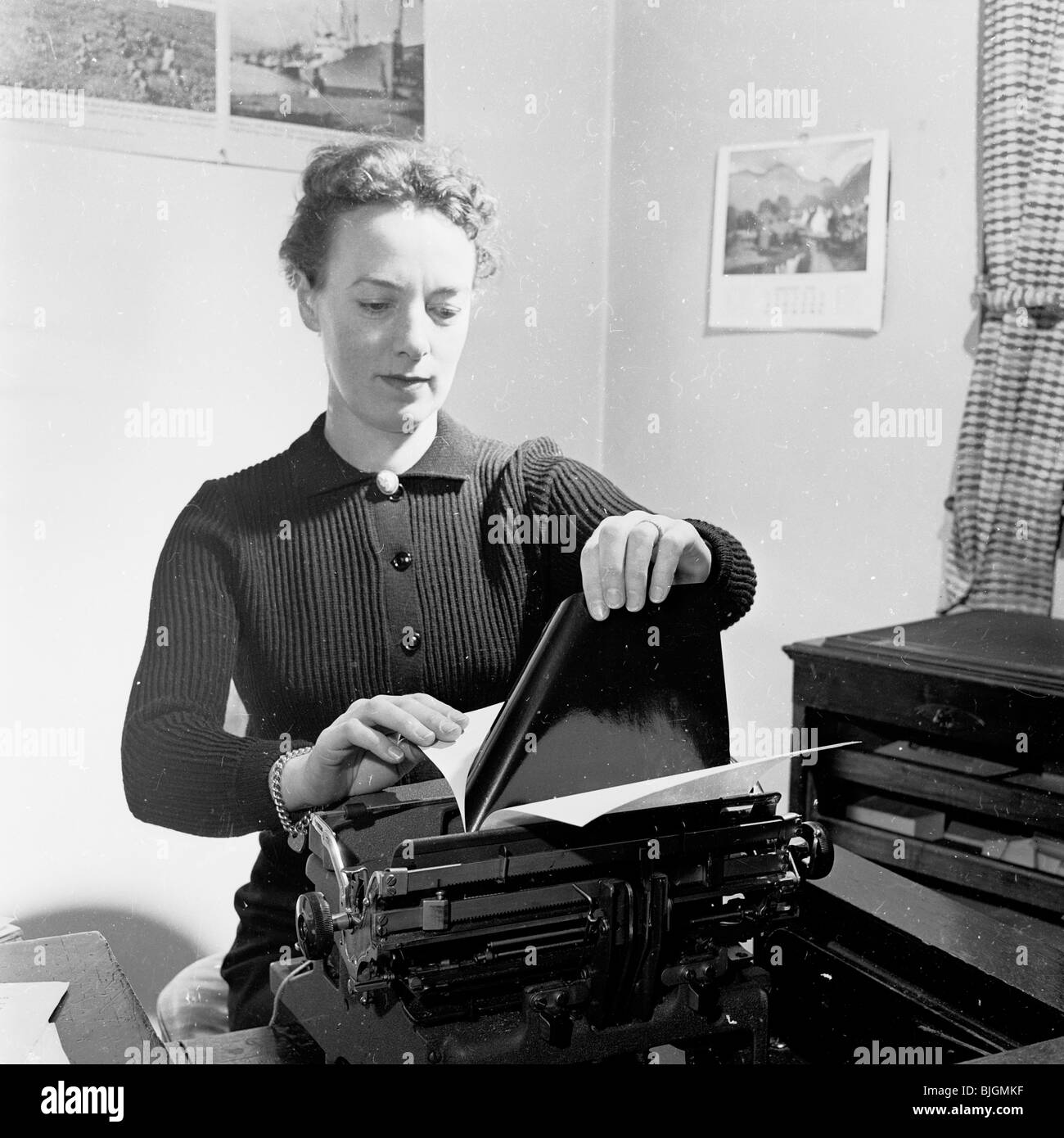 Office Typist,1950, Inghilterra. Donna segretario verifica della copia di carbonio su una lettera aziendale nella sua macchina da scrivere. Foto Stock