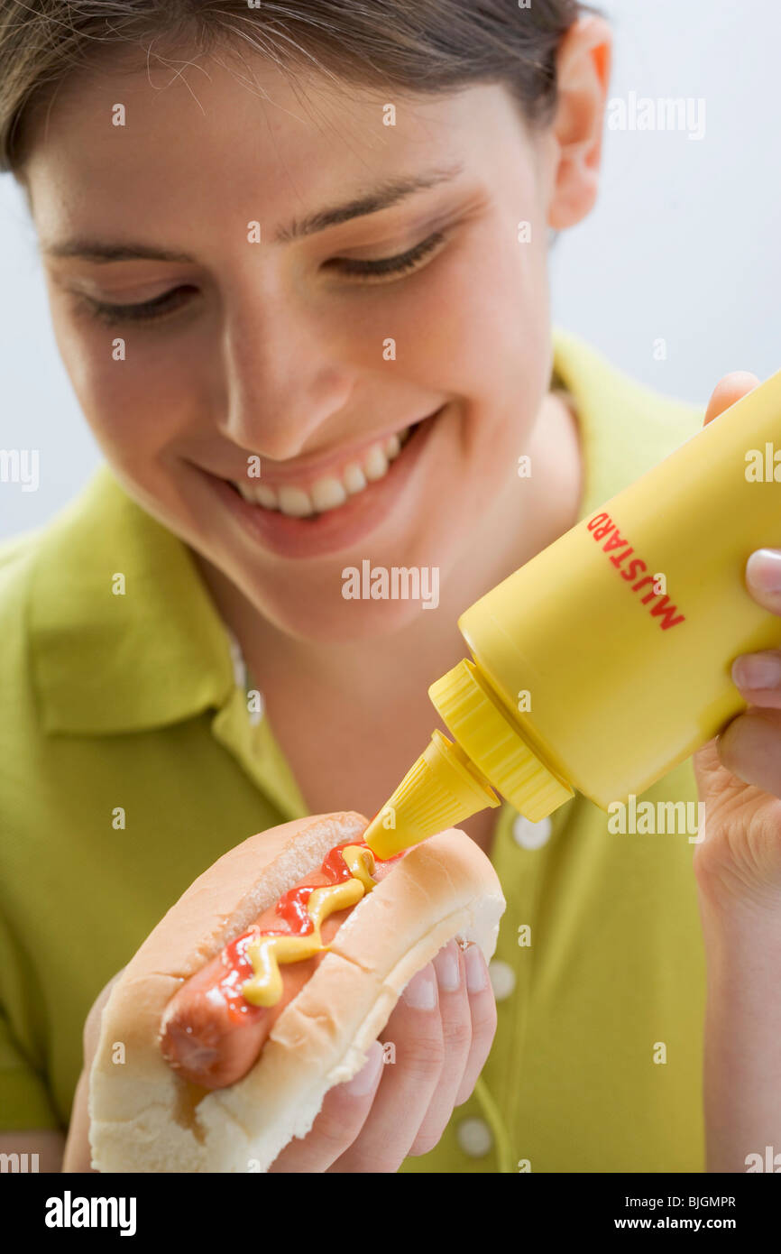 Giovane donna mettendo la senape su hot dog - Foto Stock