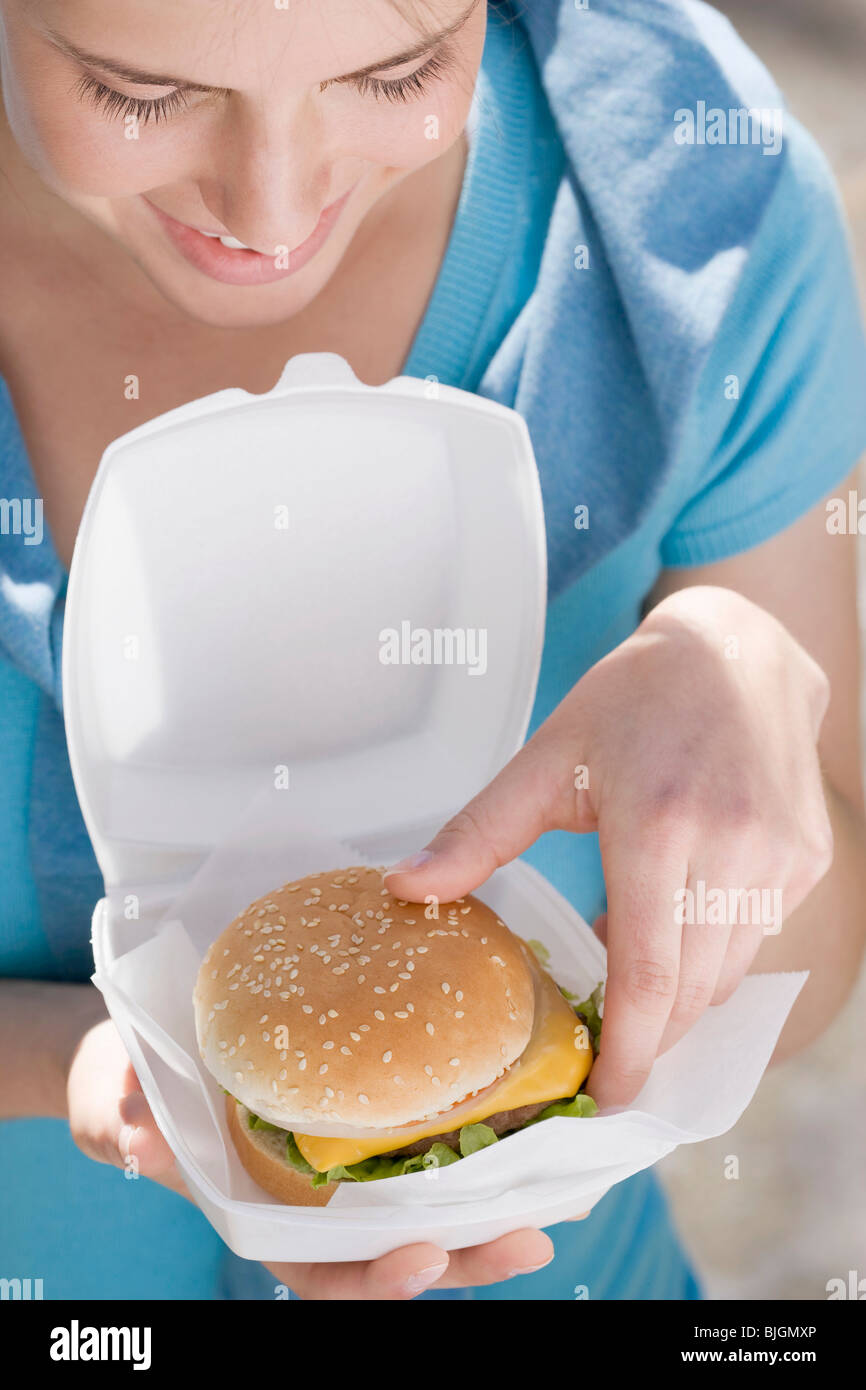 Giovane donna prendendo cheeseburger di polistirolo box - Foto Stock