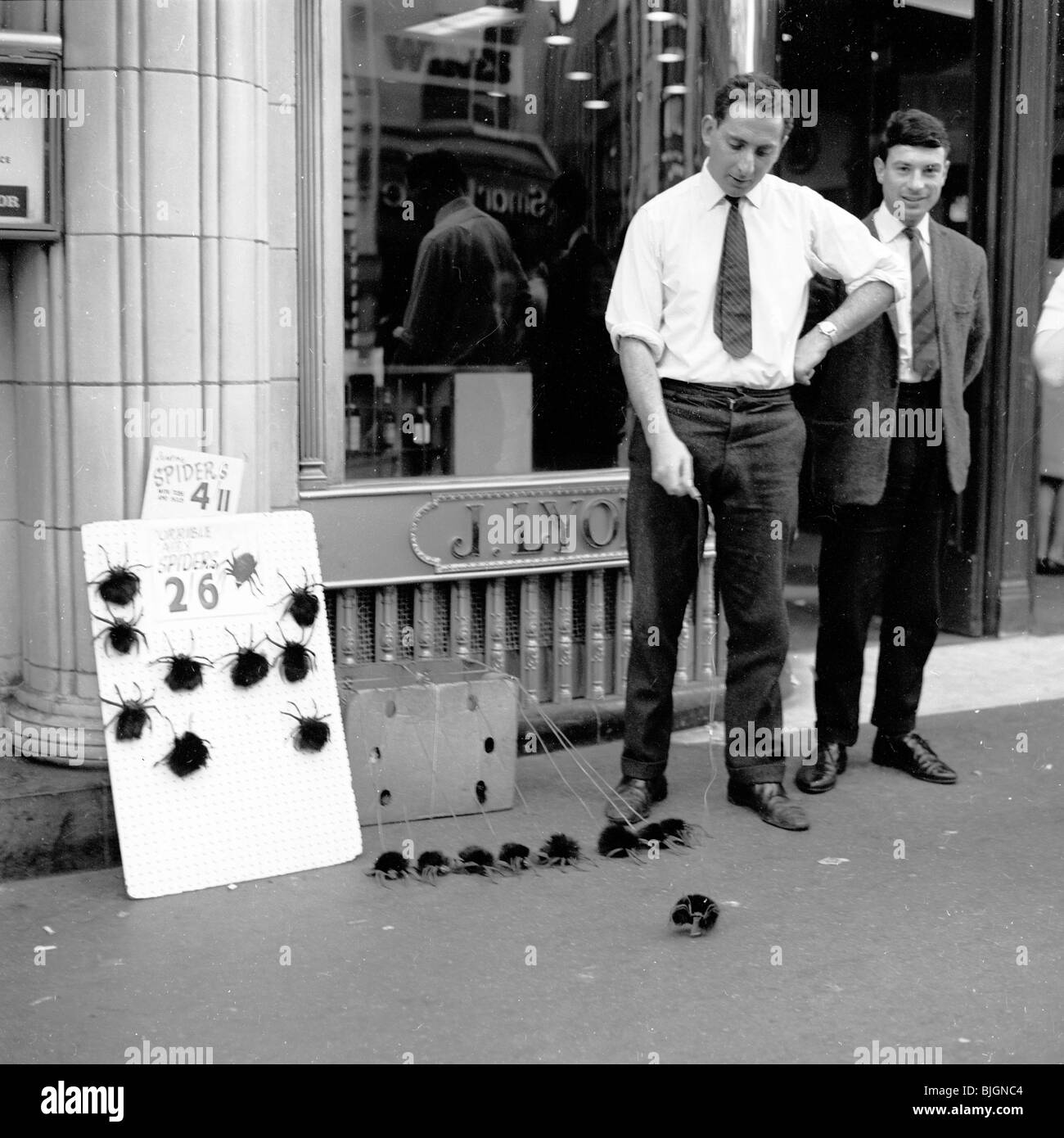 In piedi su un marciapiede, un uomo che vende peluche e giocattoli morbidi simili a ragno fuori da una caffetteria J.Lyons, Leicester Square, Londra, Inghilterra, anni '50. Foto Stock
