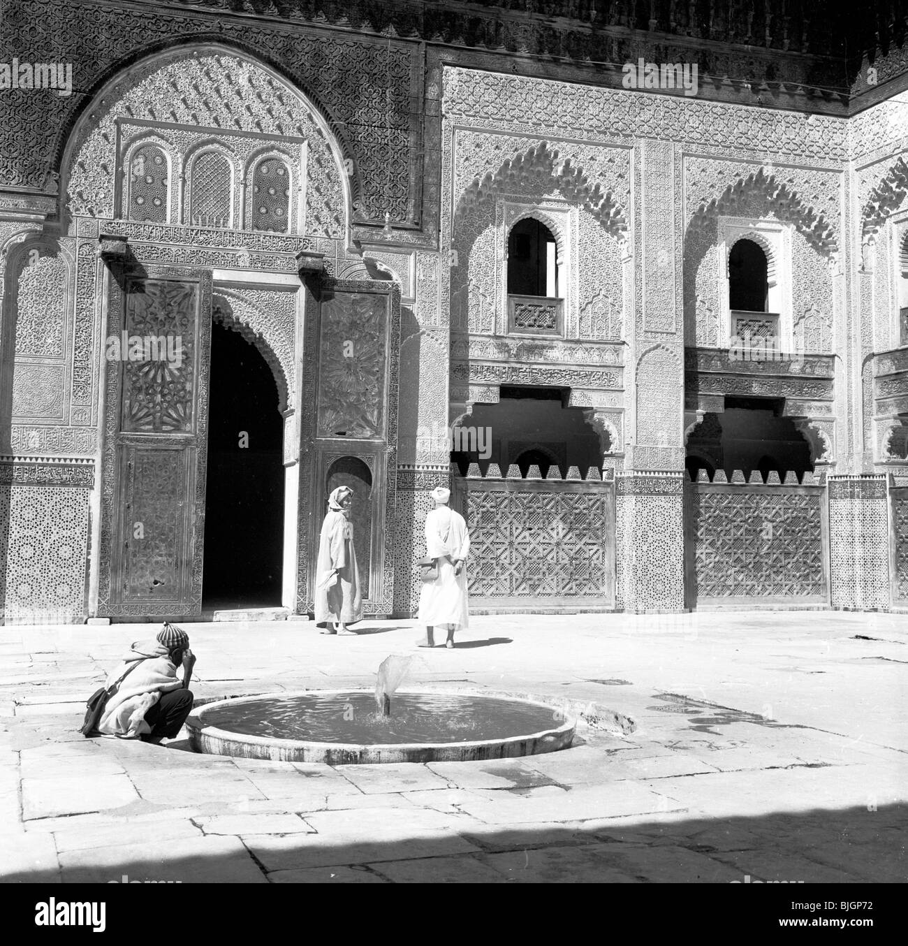 Un uomo si inginocchia dalla piccola fontana e bagni la sua testa in un cortile in una moschea, Marocco, degli anni cinquanta in questa immagine da J. Allan contanti. Foto Stock