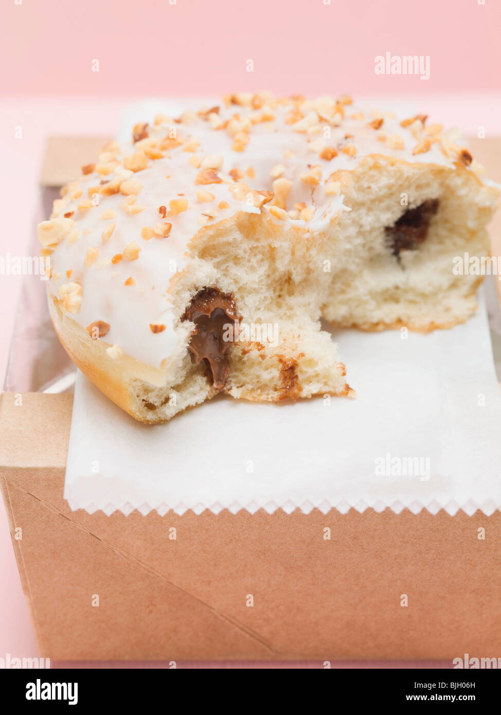 Iced ciambella con ripieno di cioccolato e noci tritate, un morso preso - Foto Stock