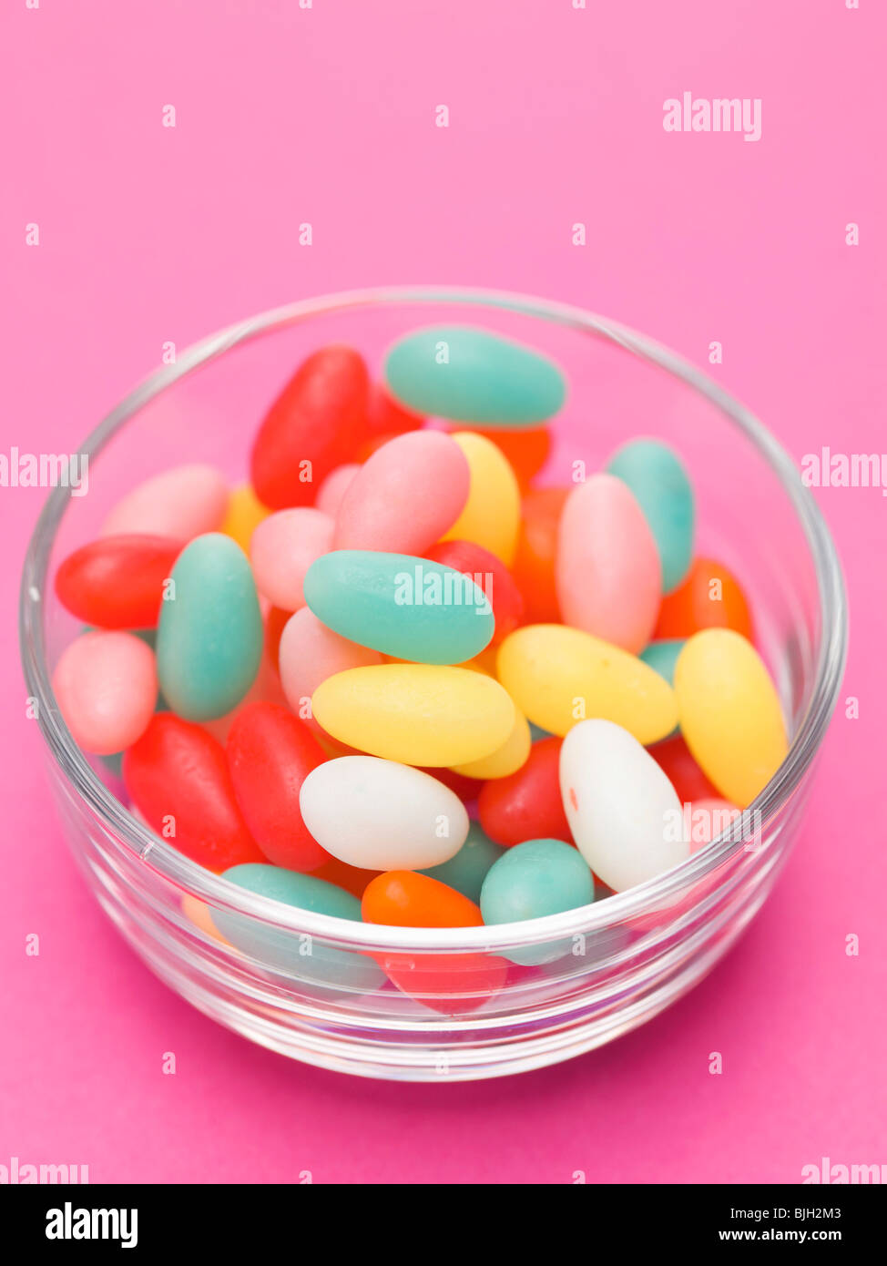 Zucchero colorato le uova in capsula di vetro, sfondo rosa - Foto Stock
