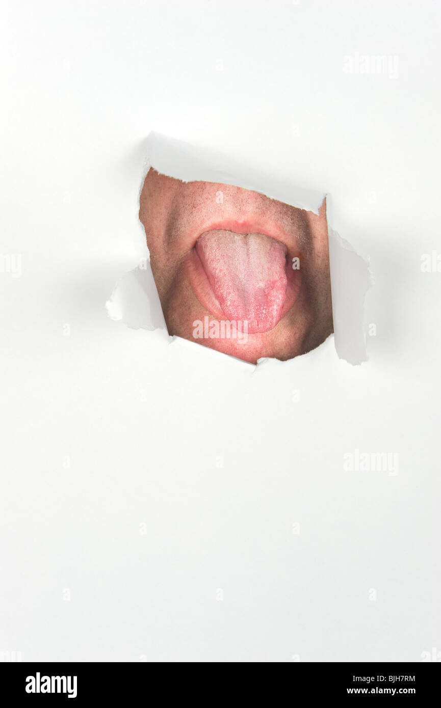Un uomo gli blocca la lingua fuori attraverso un foro in presenza di frammenti di carta. Foto Stock
