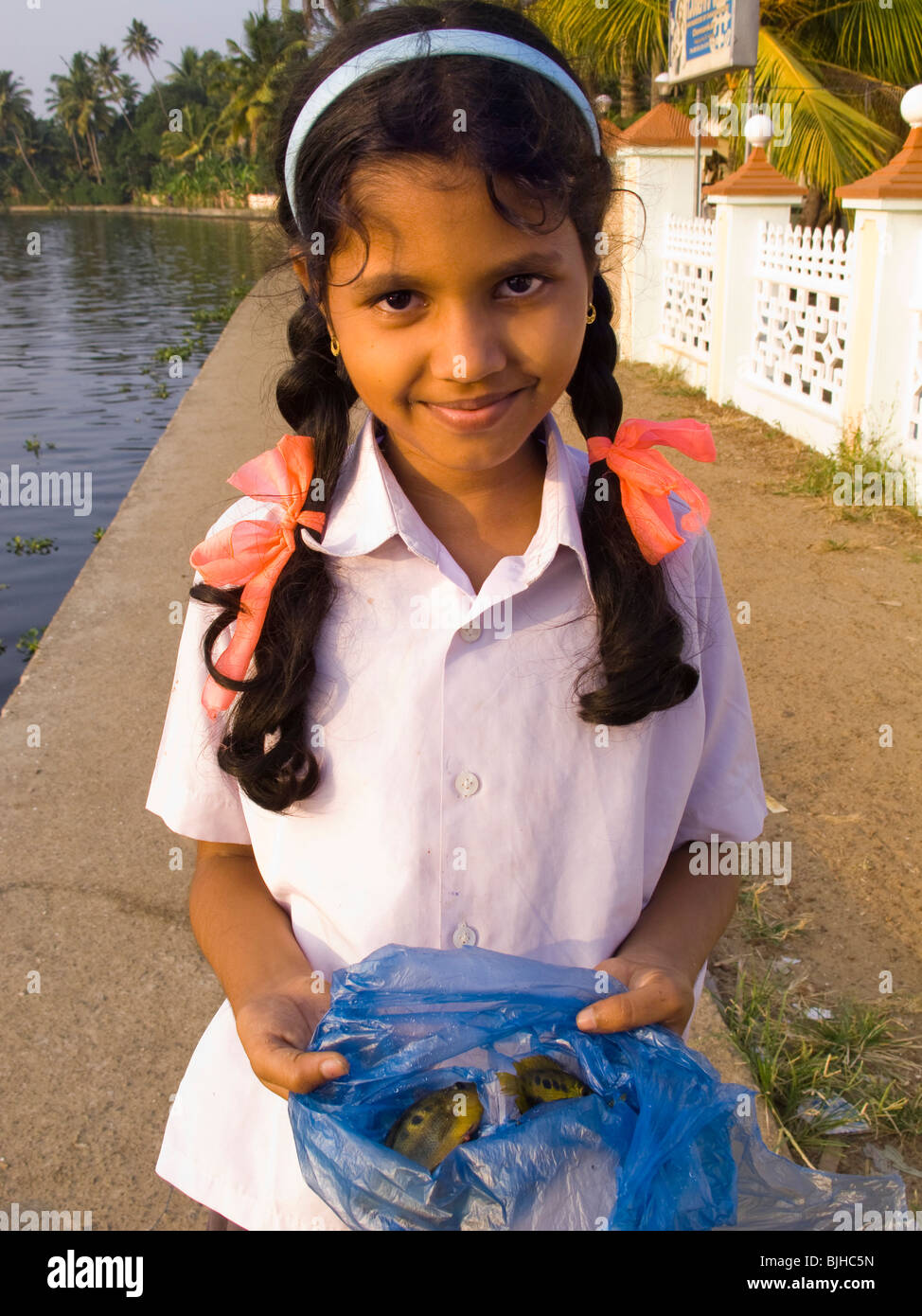 India Kerala, Alappuzha, Chennamkary, lagune, giovane ragazza che mostra il pesce catturato in fondali bassi vicino al lungofiume Foto Stock