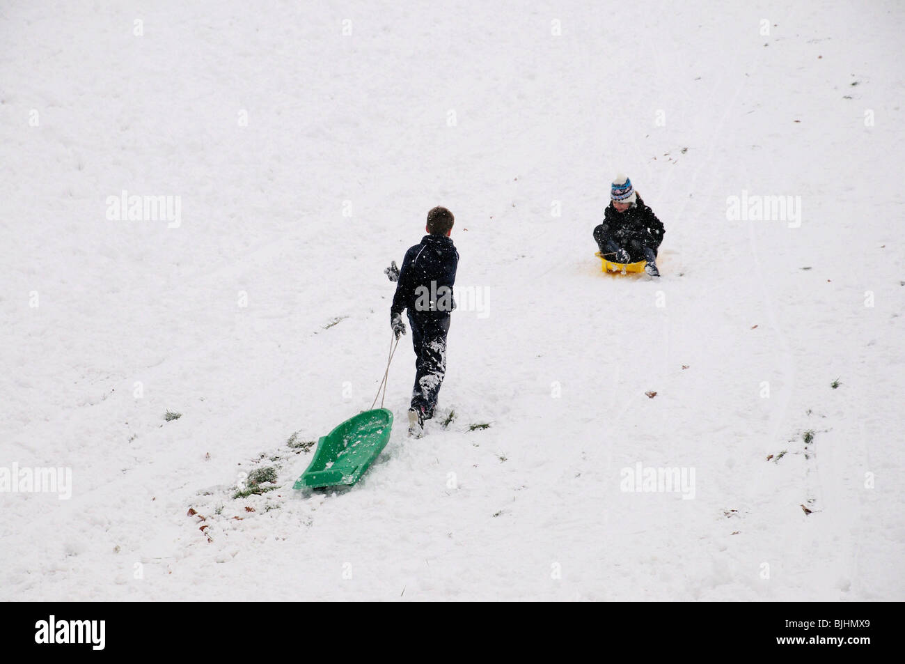 Due ragazzi di slittare verso il basso snowy hill Foto Stock