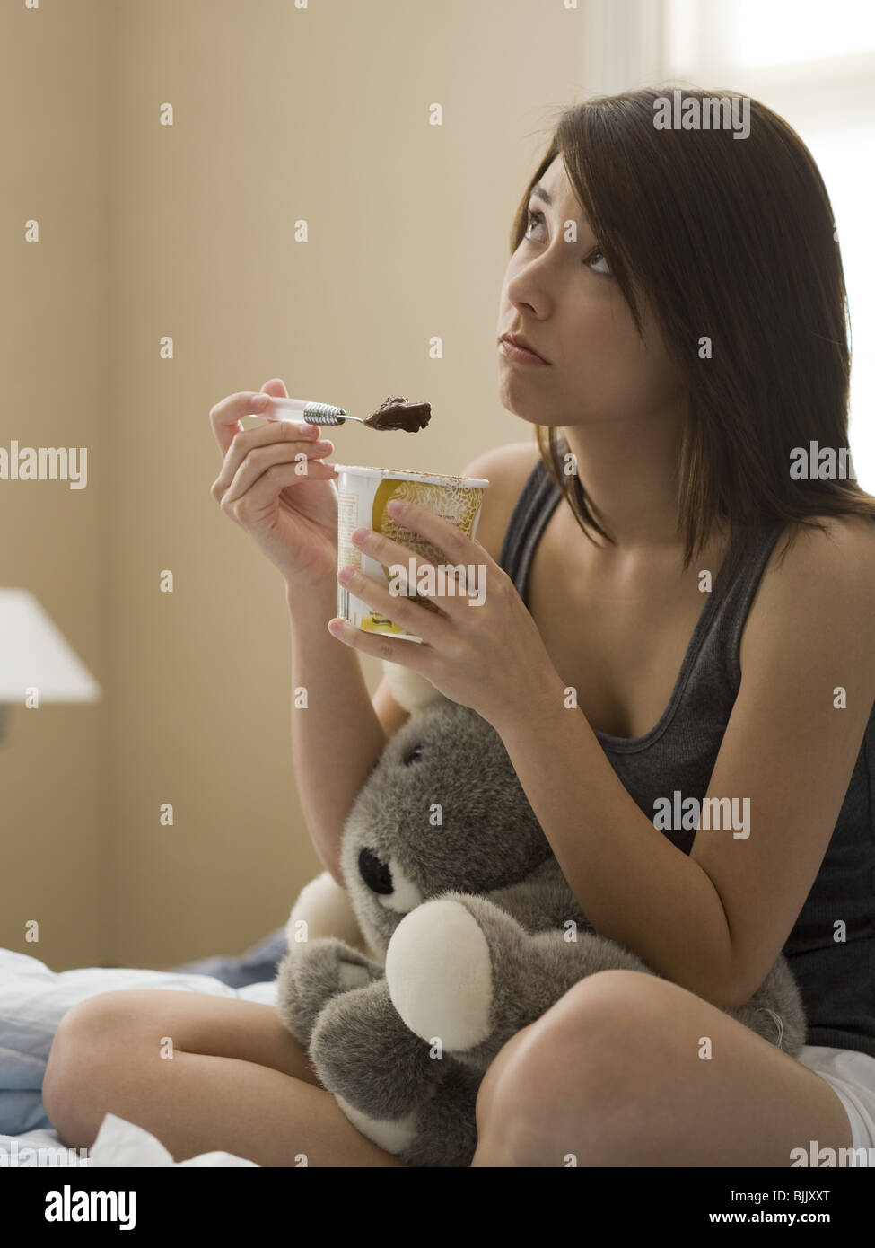 Donna di mangiare il gelato al cioccolato in letto con animali impagliati Foto Stock