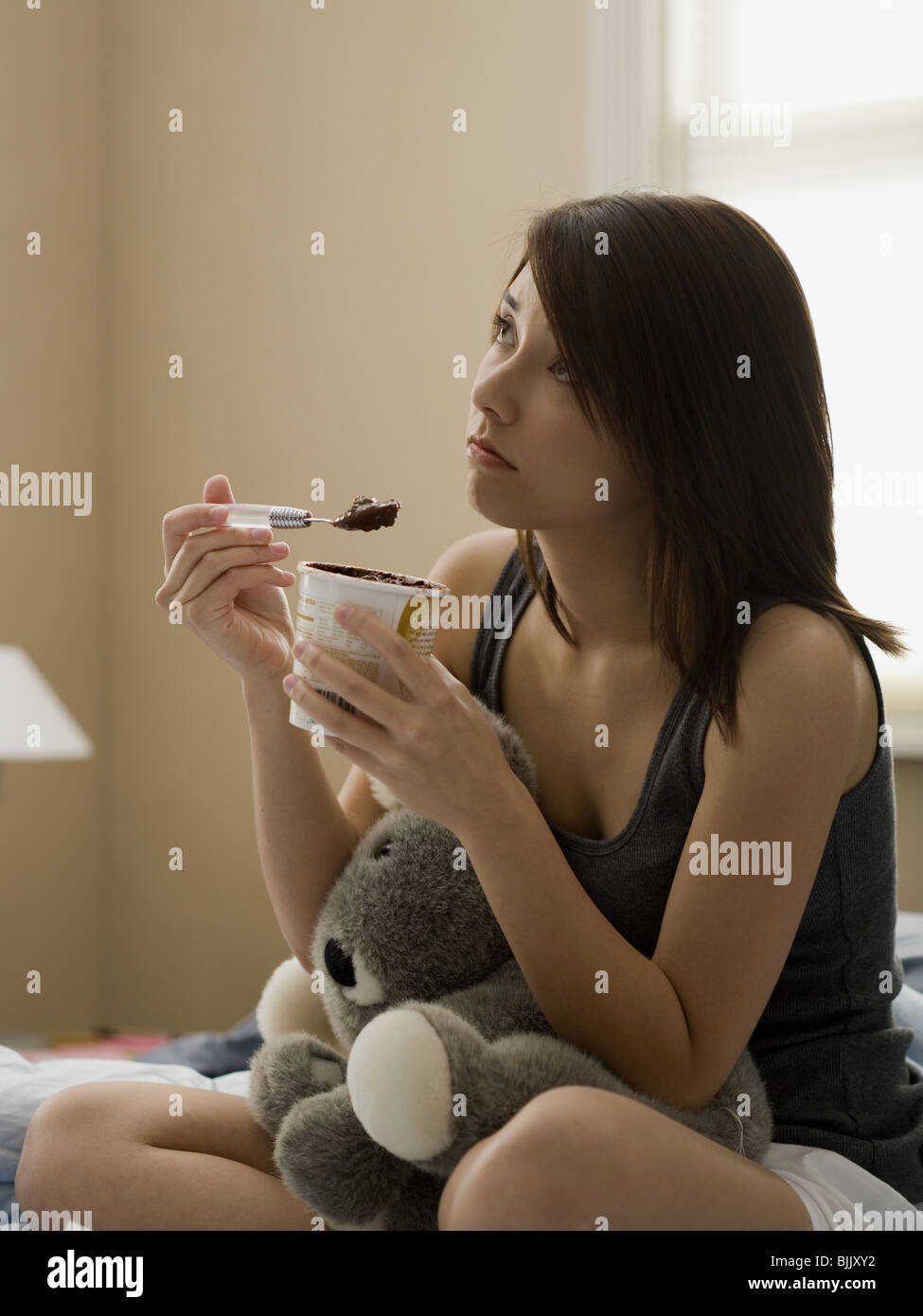 Donna di mangiare il gelato al cioccolato in letto con animali impagliati Foto Stock