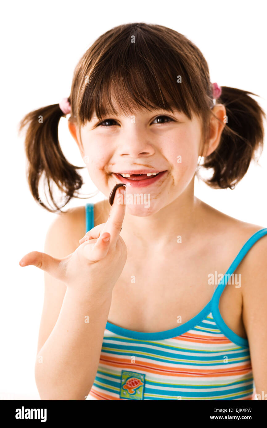 Bambina con pig-tail leccare il cioccolato il suo dito Foto Stock