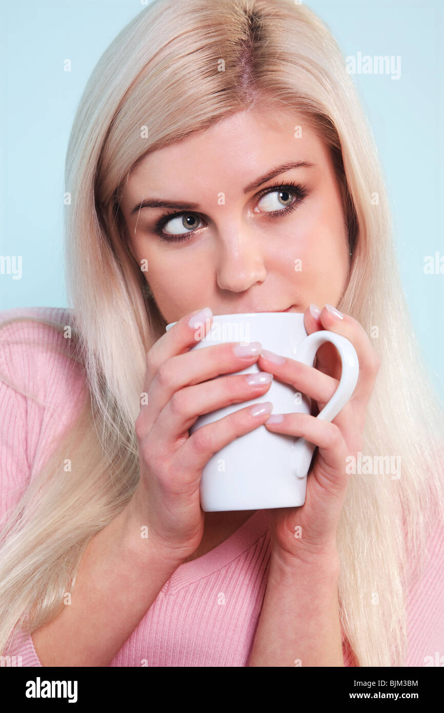Una donna bionda di bere una tazza di tè guardando fuori del telaio. Foto Stock