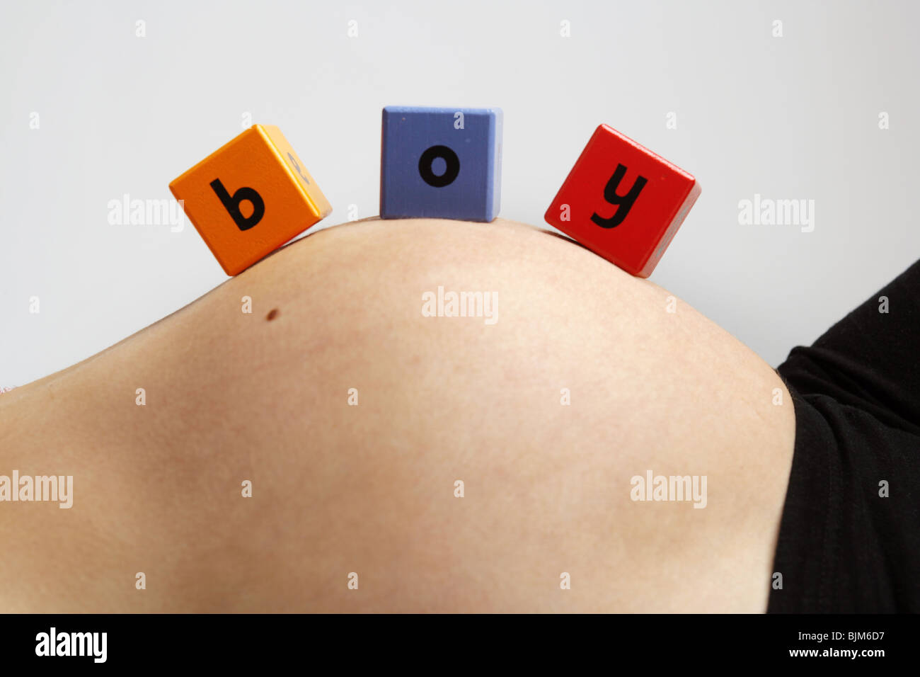 Nove mesi di gravidanza della donna sdraiata sulla schiena con il giocattolo di legno blocchi sul suo ventre ragazzo di ortografia Foto Stock