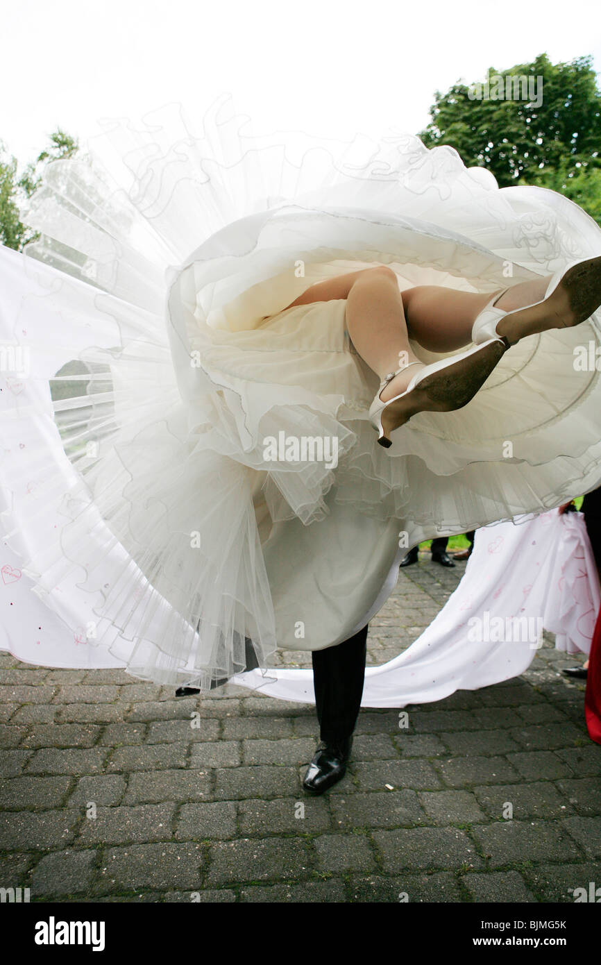 Lo sposo portando la sua sposa attraverso il cuore di un foro sagomato in un lenzuolo, nozze personalizzati, vista da sotto l'abito da sposa Foto Stock