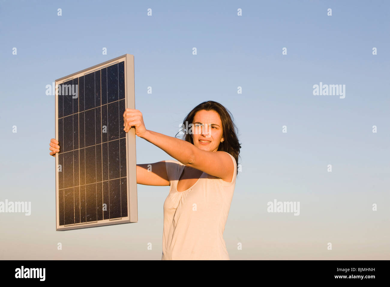 Donna che mantiene un pannello solare di fronte a un cielo blu Foto Stock