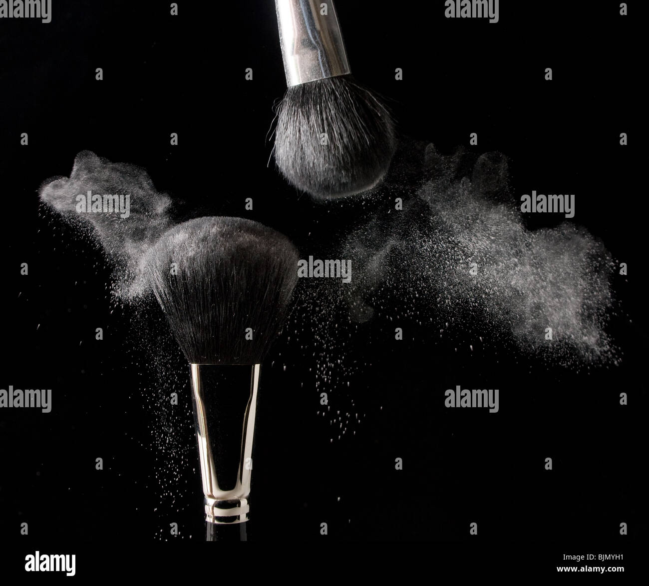 La polvere viene strofinato via due cosmetici spazzole su uno sfondo nero Foto Stock