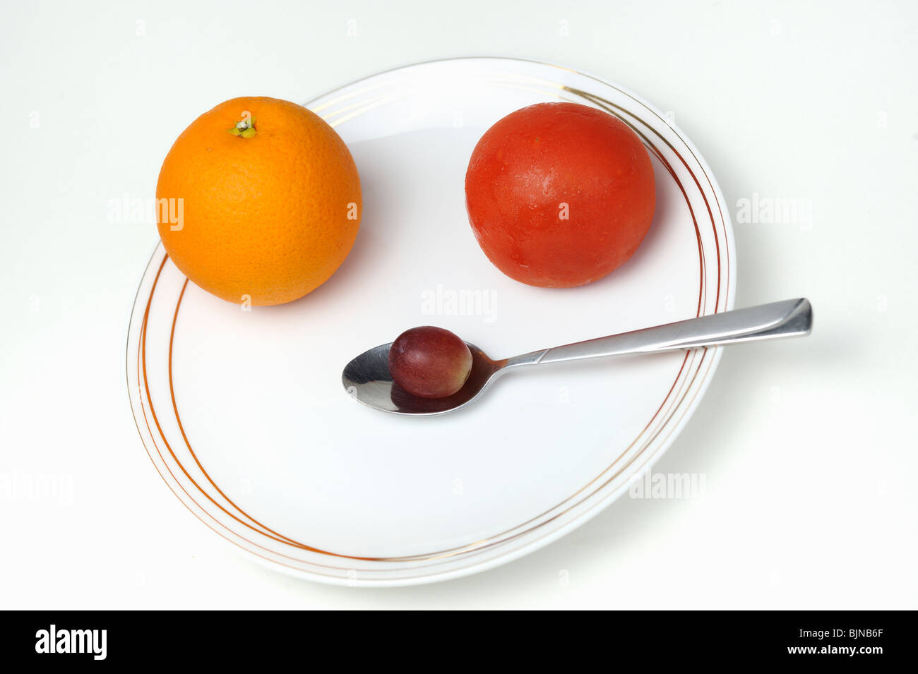 Piastra e cucchiaio con uno arancione, uno tomatoe, uno uva, su sfondo bianco Foto Stock