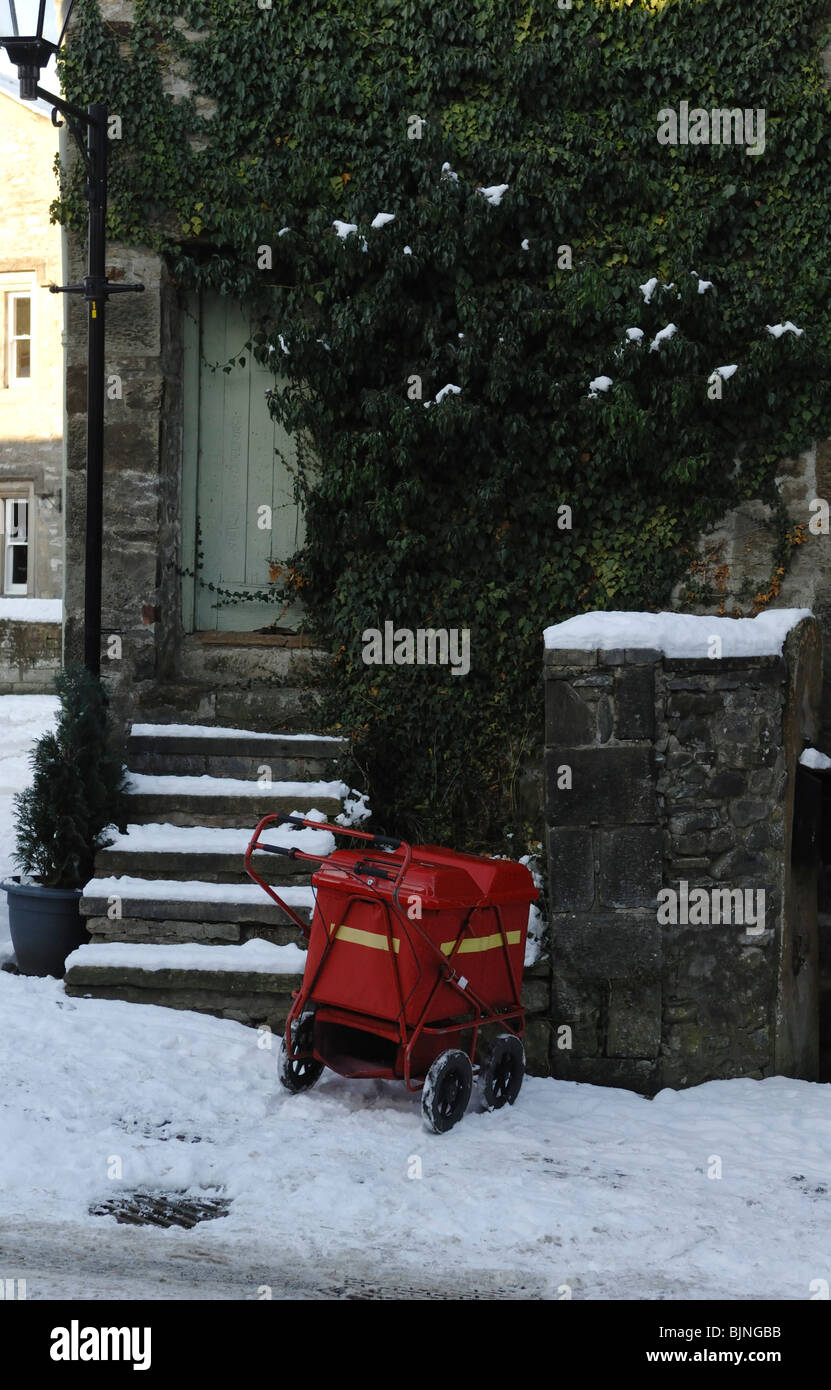 A Royal Mail delivery carrello fuori un lato coperto di edera cottage su una coperta di neve lane. Foto Stock