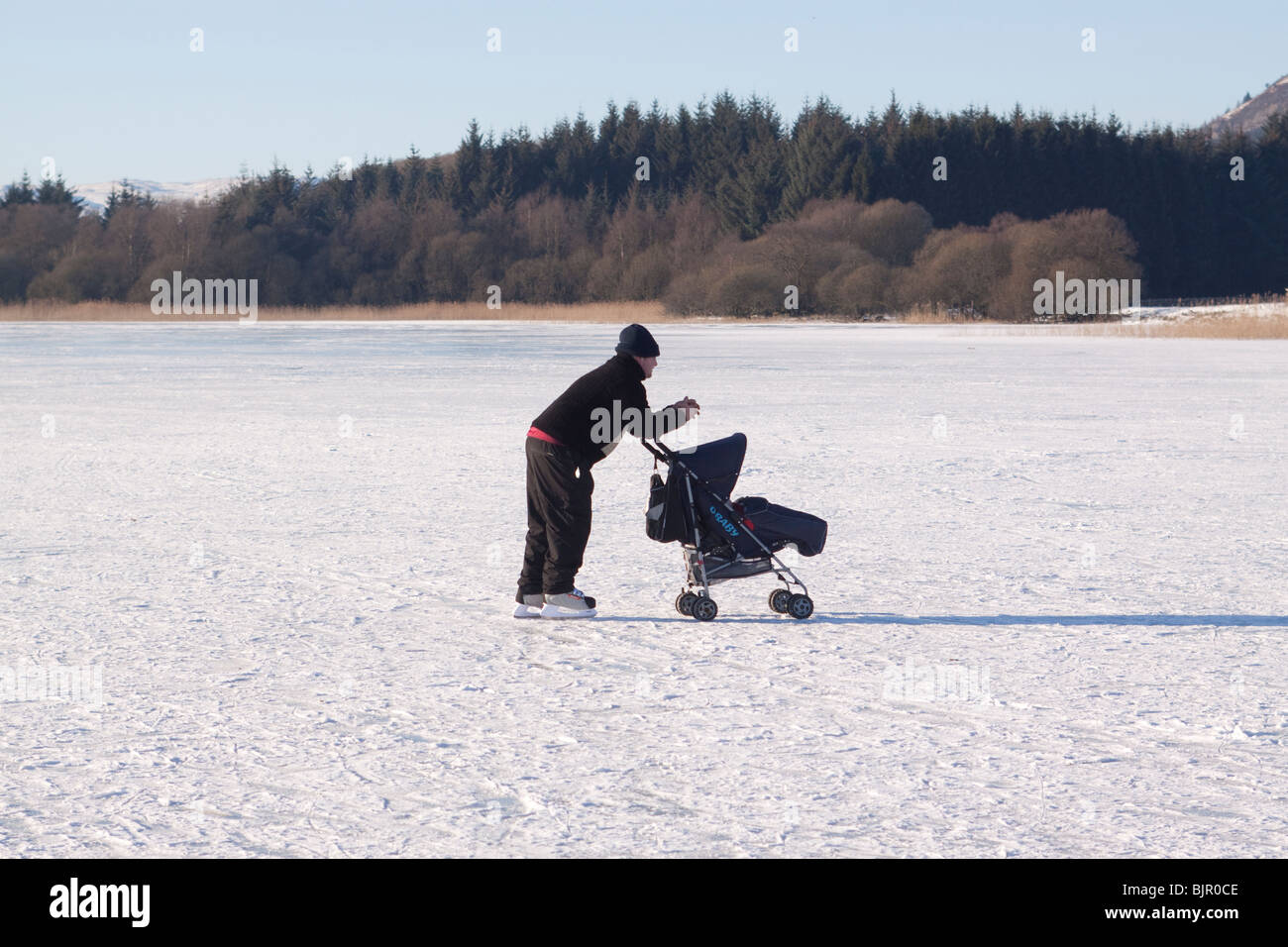 Pattinatore su ghiaccio spingendo la PRAM sul lago ghiacciato Foto Stock