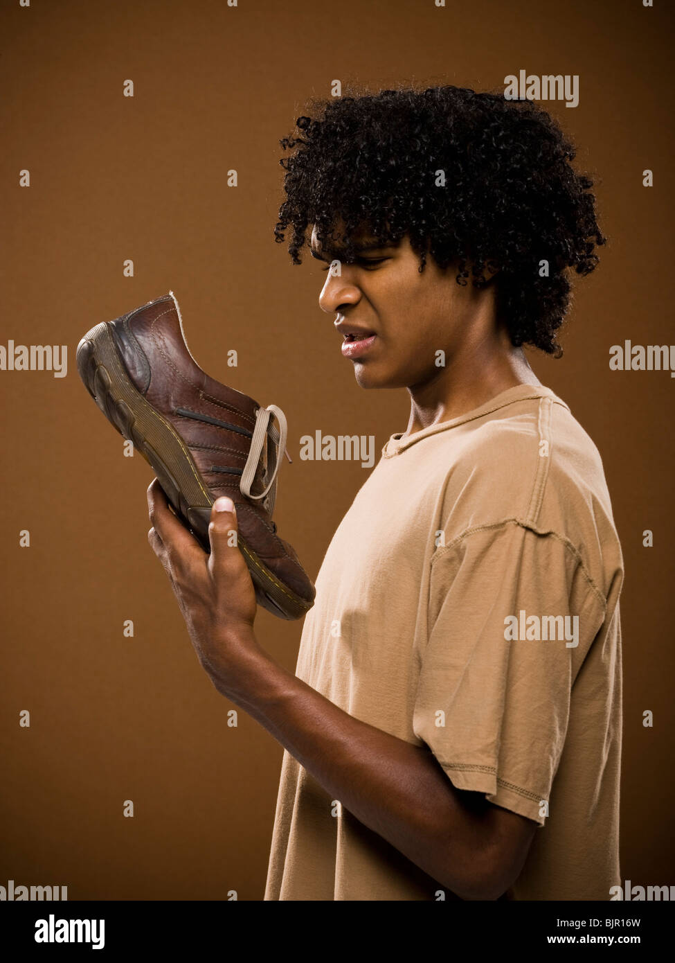 Giovane uomo in una maglietta marrone in possesso di una scarpa e il suo naso. Foto Stock