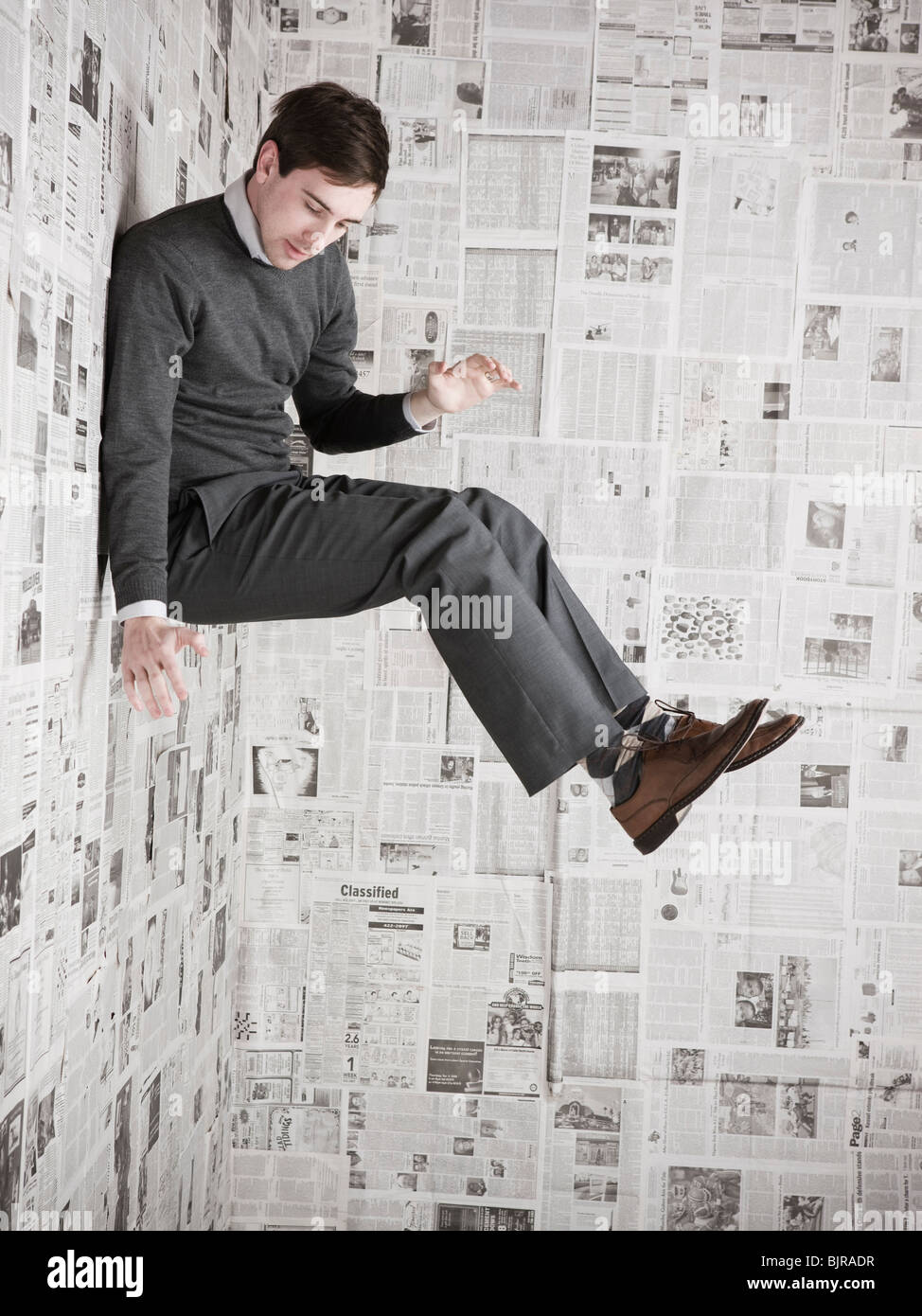 Giovane uomo incollato alla parete ricoperta di quotidiani, studio shot Foto Stock