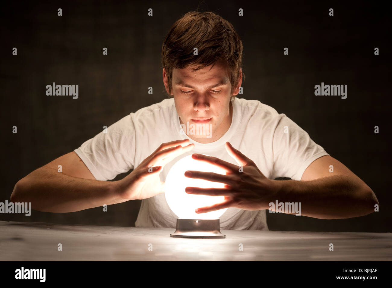 Studio shot del giovane con le mani attorno a incandescente sfera di cristallo Foto Stock