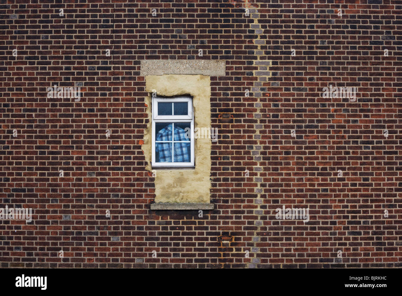 Una maglietta controllati si blocca nella finestra di un appartamento finestra, mal rifinito con cemento, amid incrinature del muro di mattoni. Foto Stock