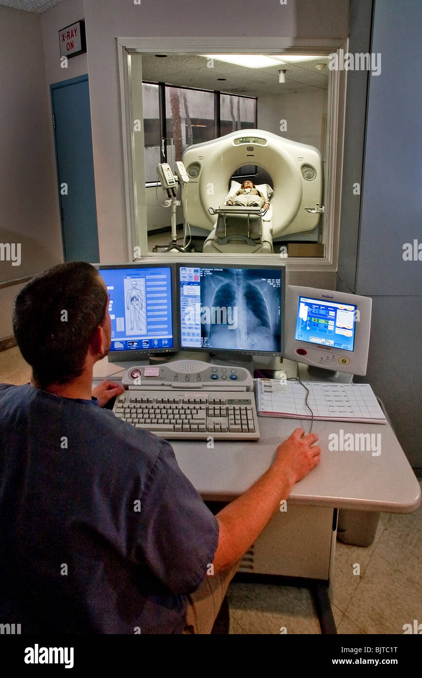 Seduto a una consolle di controllo, un operatore medico si prepara per un esame TAC a California studio radiologico. Foto Stock