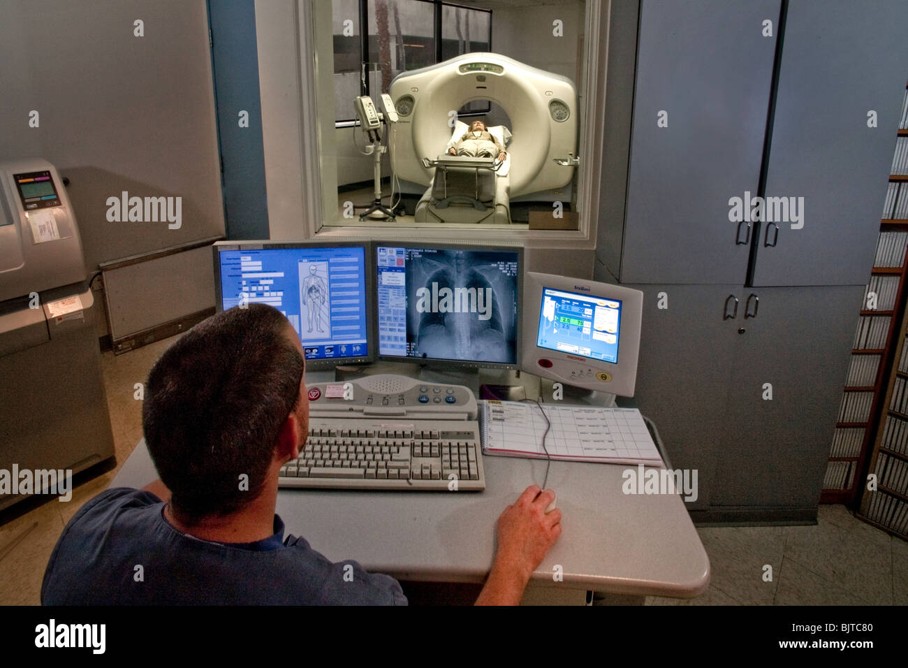 Seduto a una consolle di controllo, un operatore medico si prepara per un esame TAC a California studio radiologico. Foto Stock