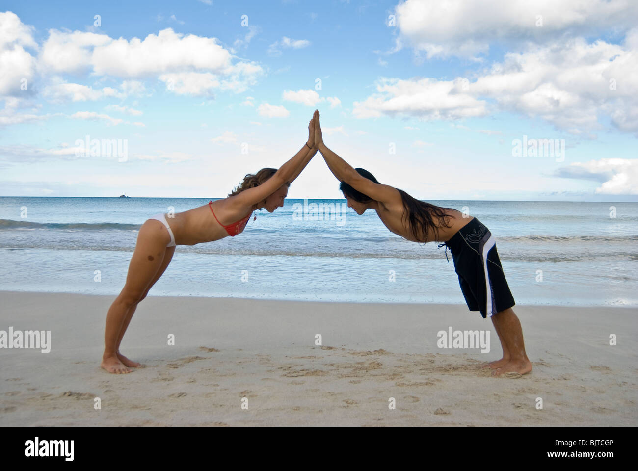 Coppia giovane ( uomo asiatico e Caucasico donna) nei primi anni venti facendo yoga partner sulla spiaggia di sabbia bianca a Hawaii Foto Stock