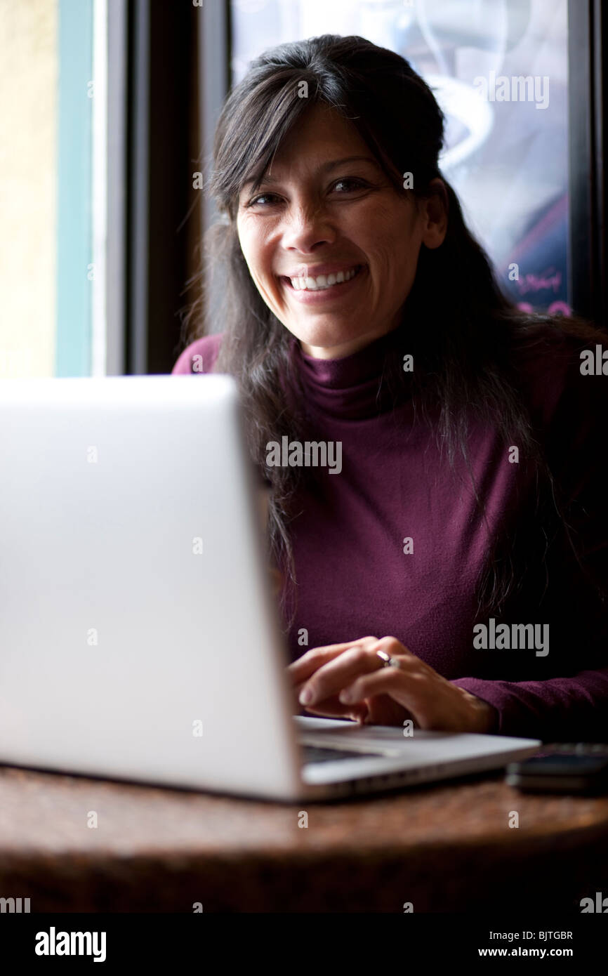 Una metà donna adulta di bere il caffè accanto al laptop in cafe Foto Stock